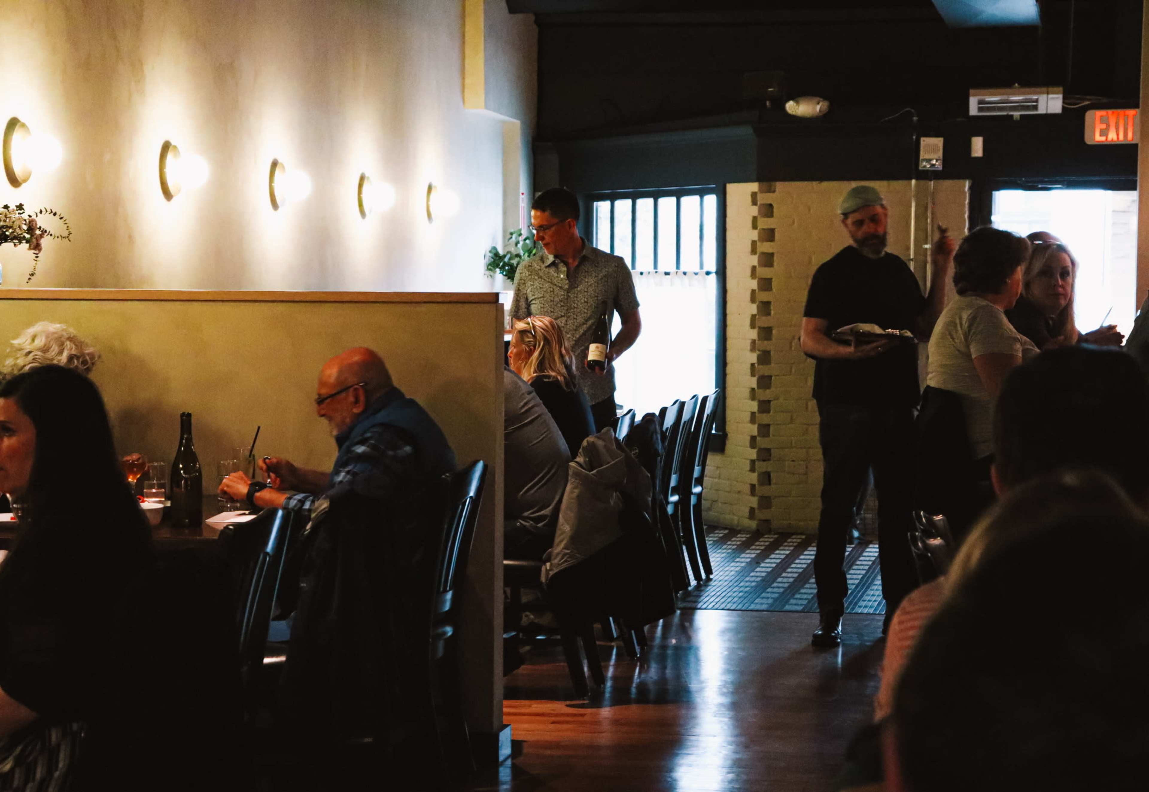 A dining establishment is filled with patrons seated at tables, while a server carrying food walks through the aisle.
