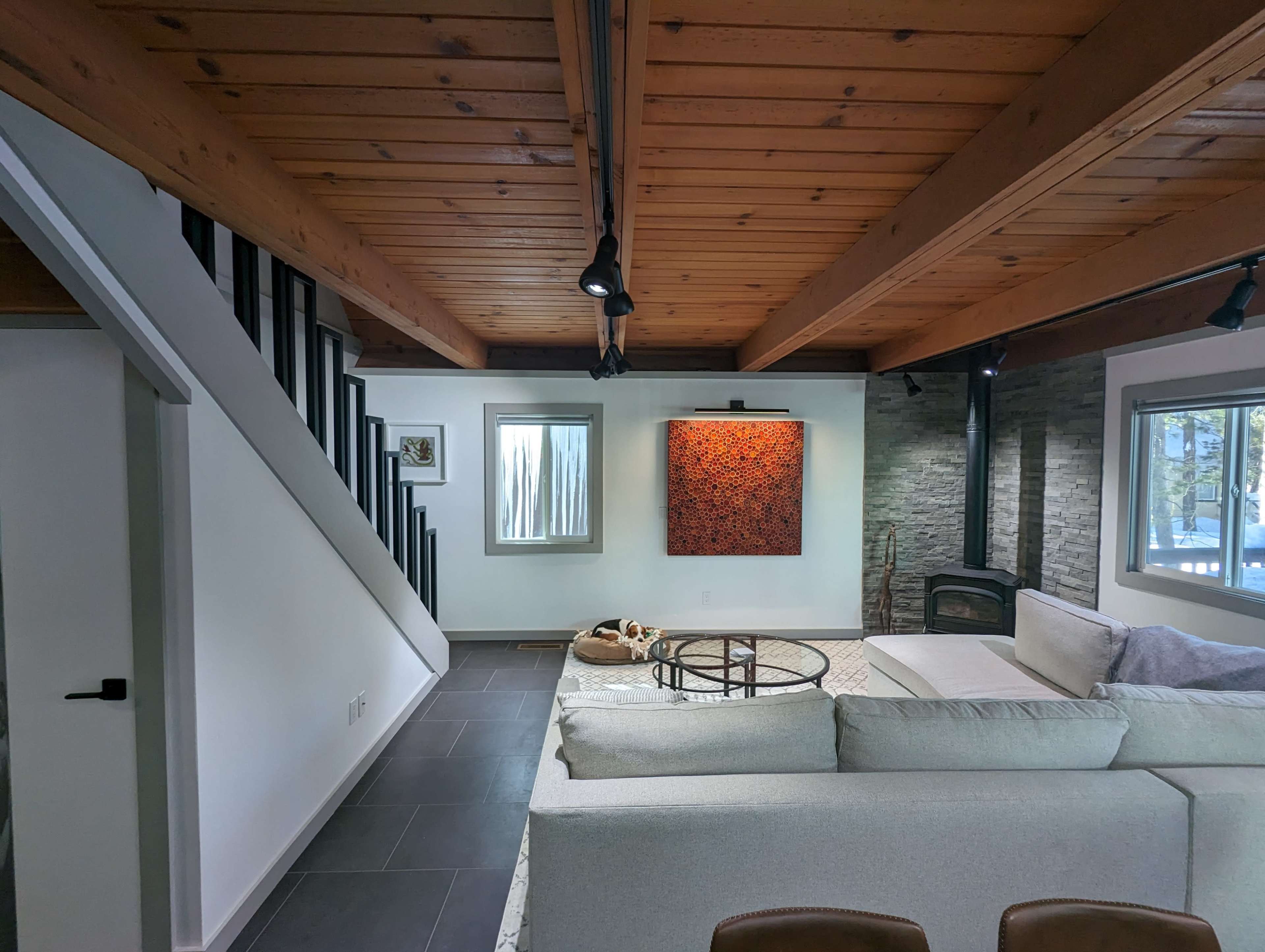 A modern living room features a large sectional sofa, a coffee table, and a piece of abstract art on the wall, with a staircase leading to an upper level.