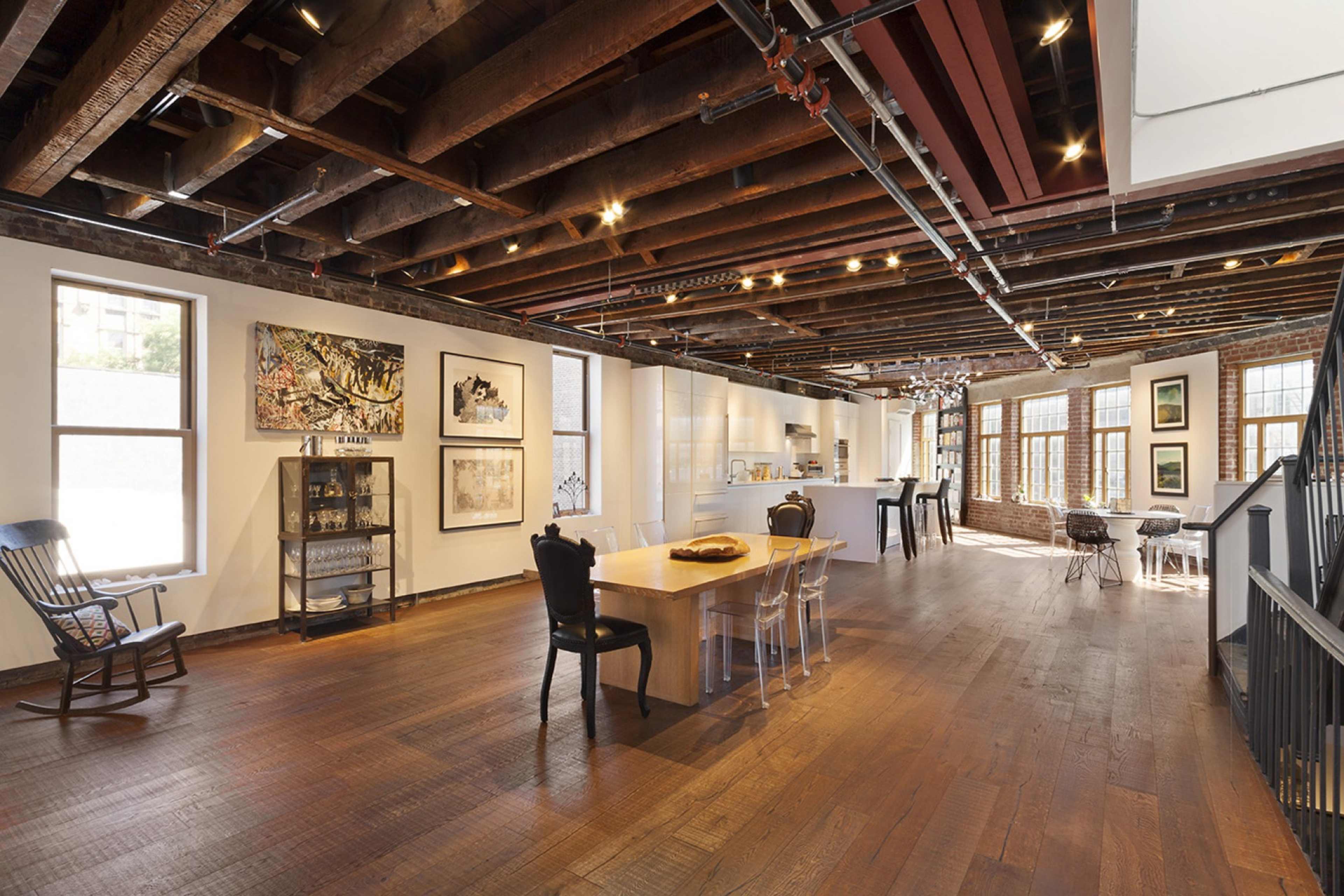 A spacious, well-lit room with wooden beams, featuring a dining table surrounded by various chairs and art pieces on the walls.