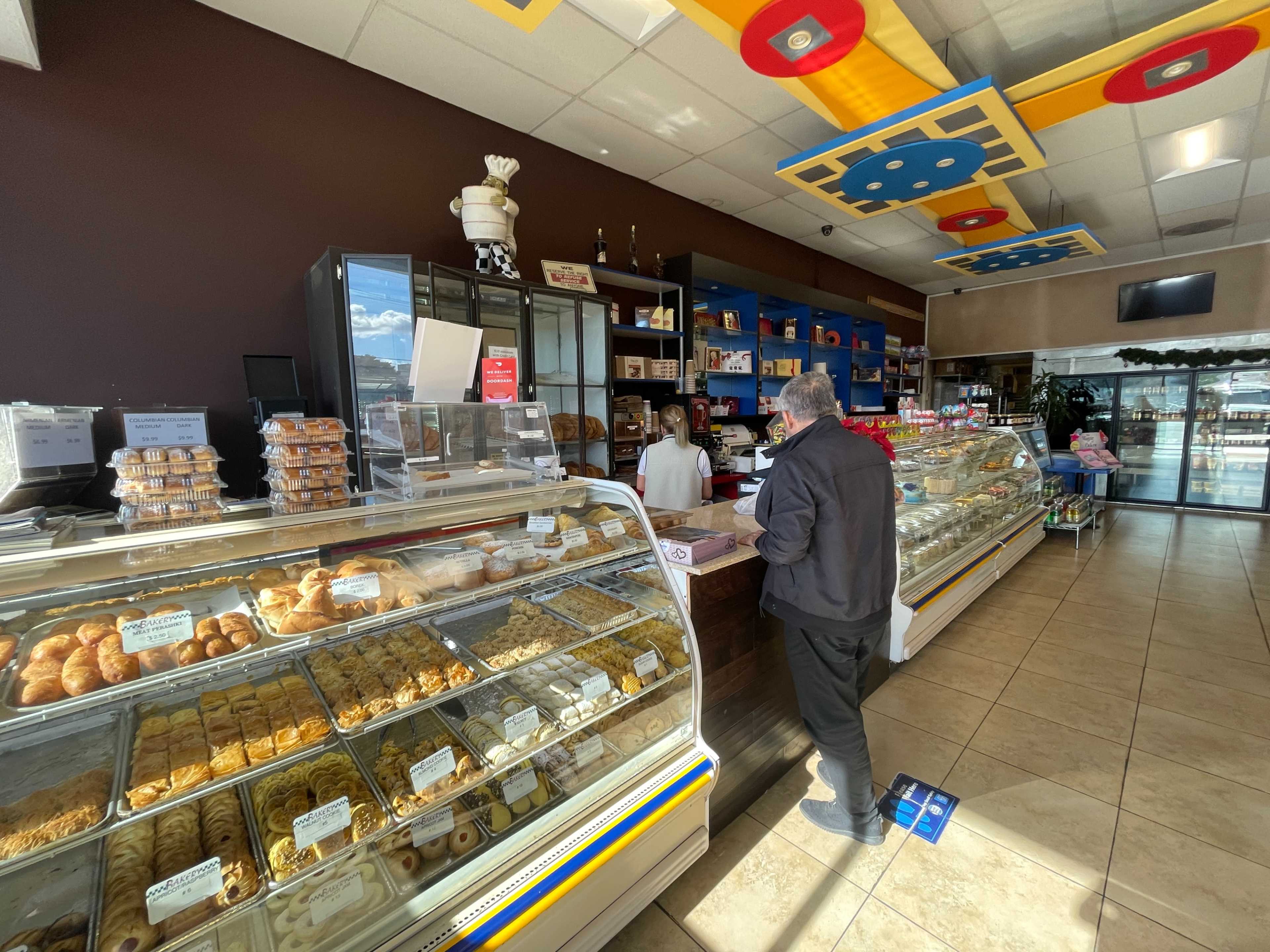 A customer stands at the counter of a pastry shop, with display cases filled with various baked goods and a staff member ready to assist.