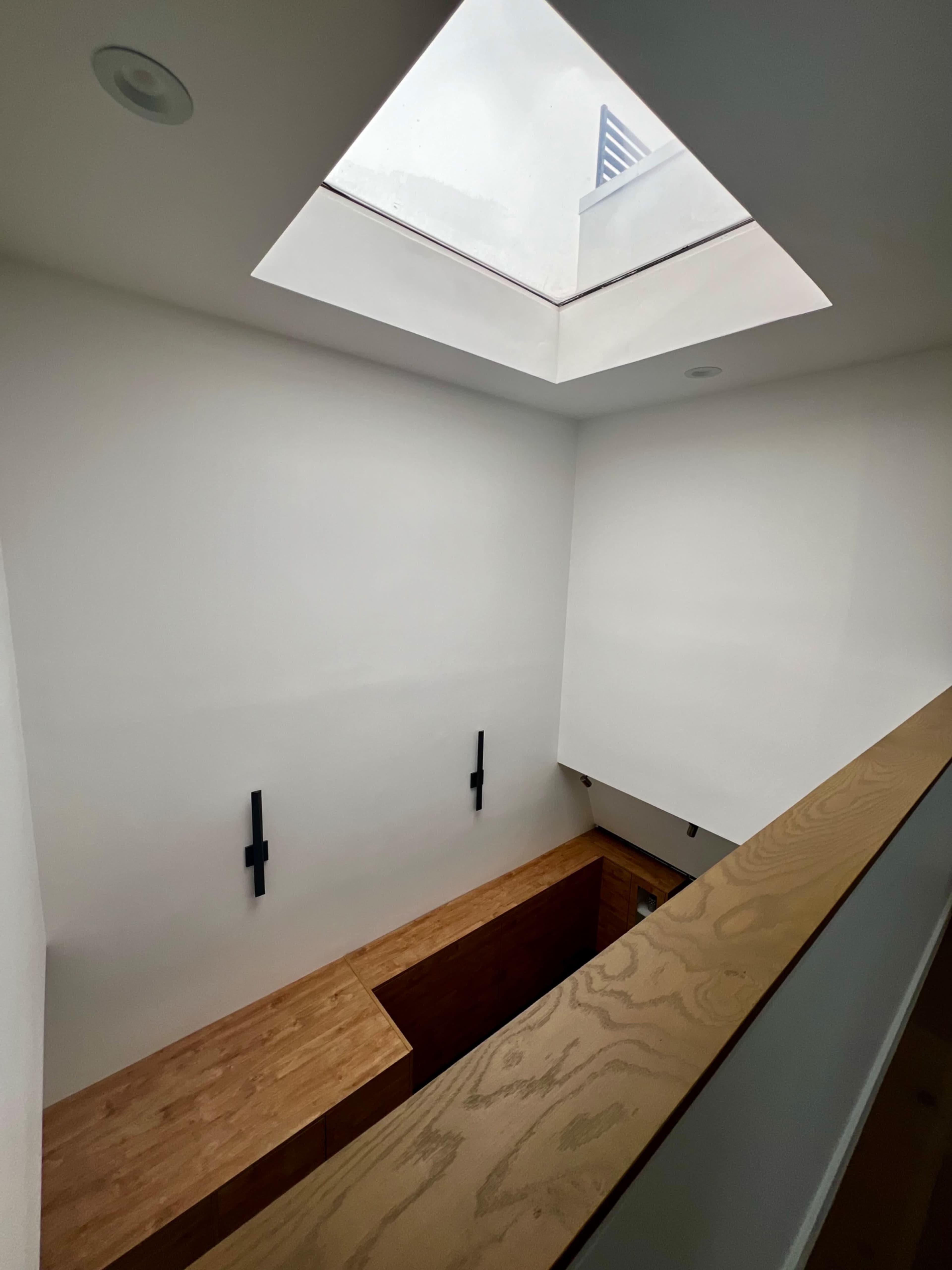 An interior space with a skylight above a wooden ledge and minimalistic white walls.