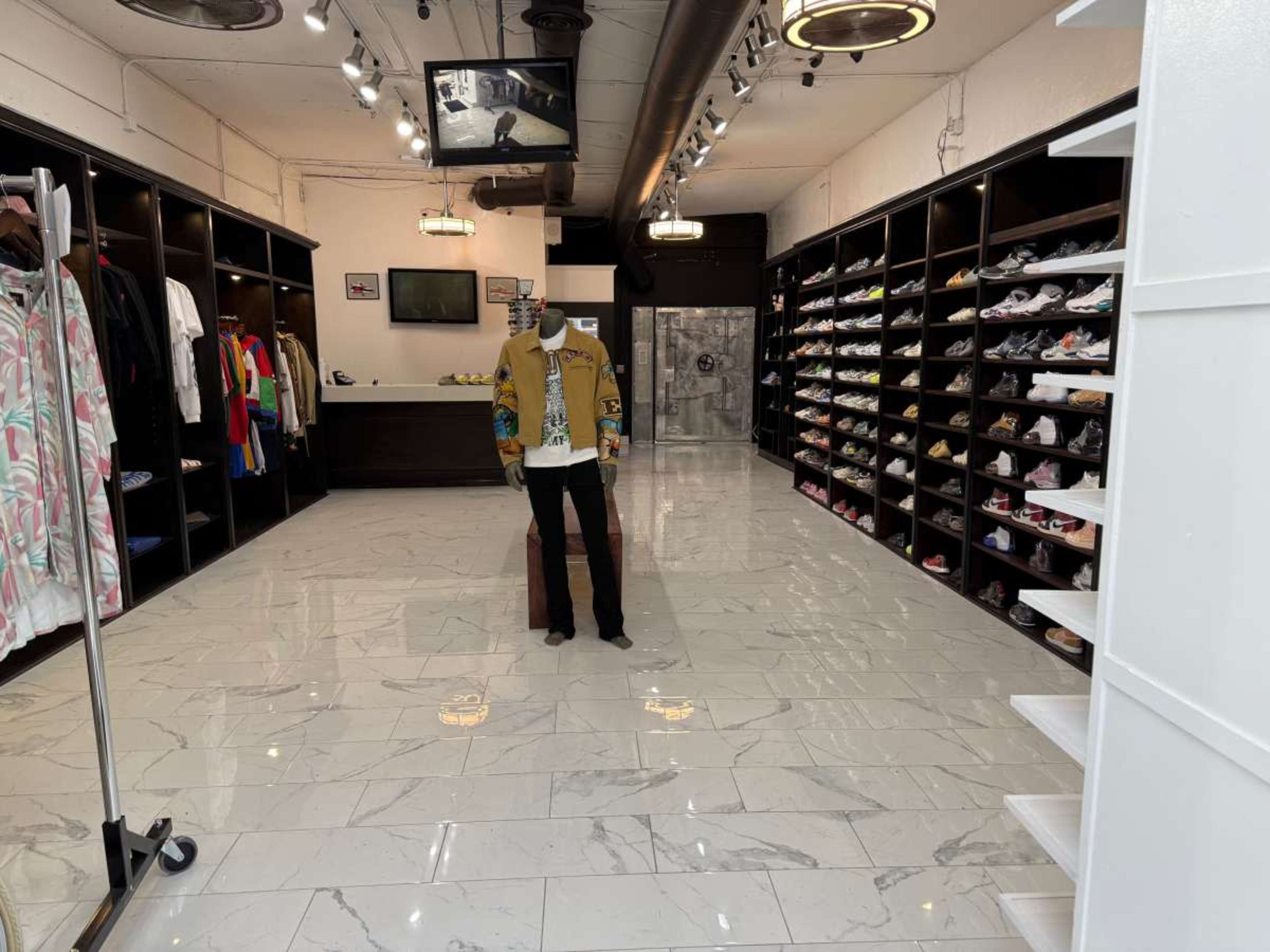 The image shows a well-organized retail store featuring clothing racks, shelves filled with shoes, and a display mannequin in the center.