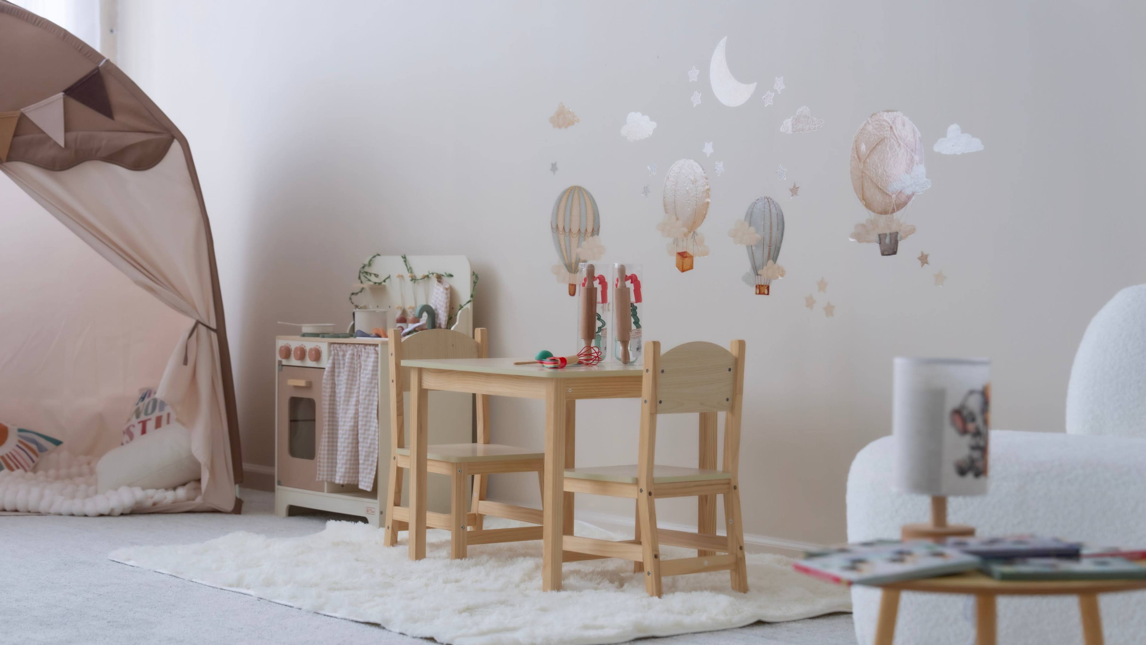 The image shows a children's playroom featuring a small wooden table and chairs set, with decorative wall art of hot air balloons and clouds.