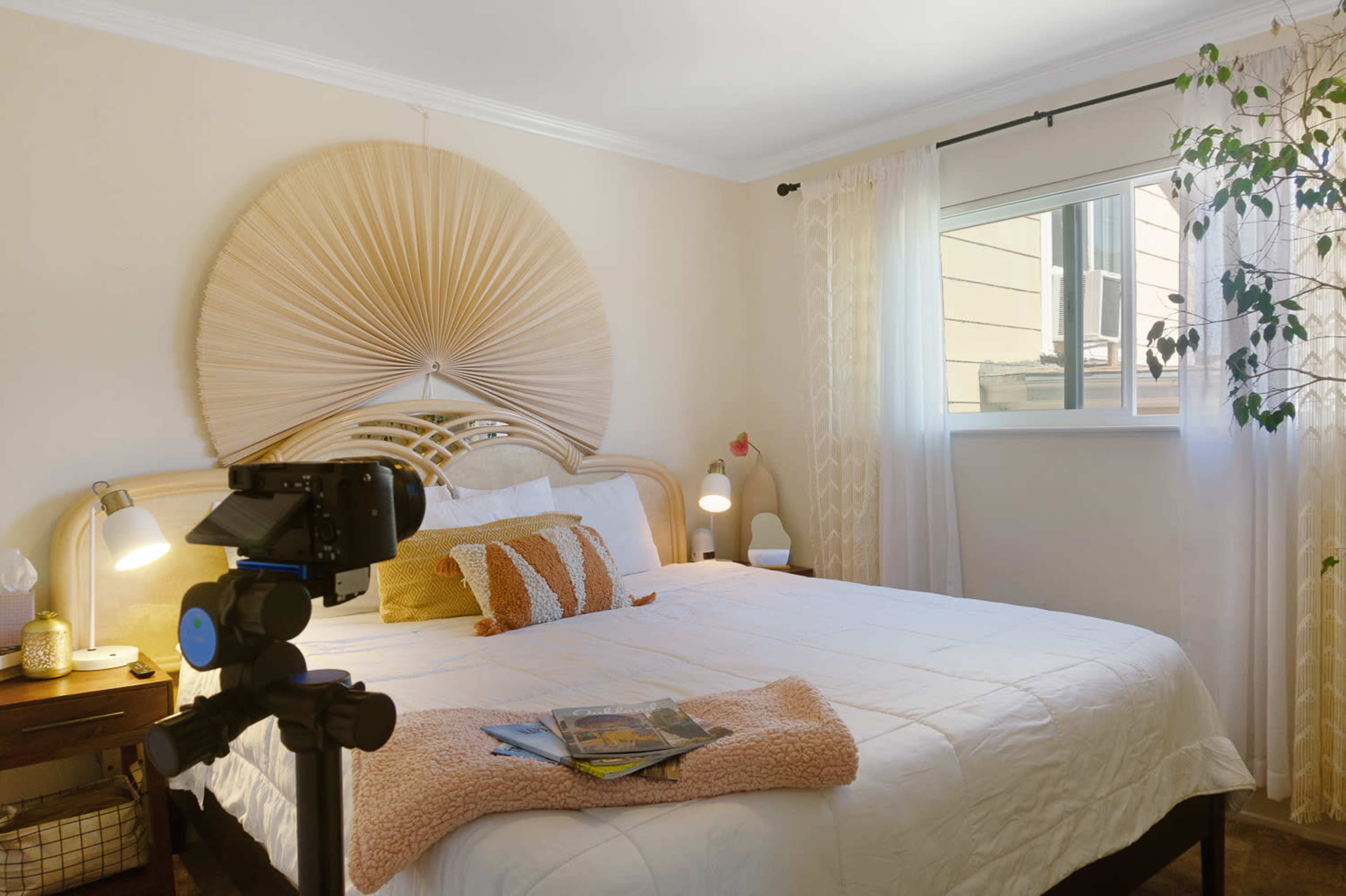 A neatly arranged bedroom with a large bed, decorative headboard, bedside lamps, and a window allowing natural light to enter.