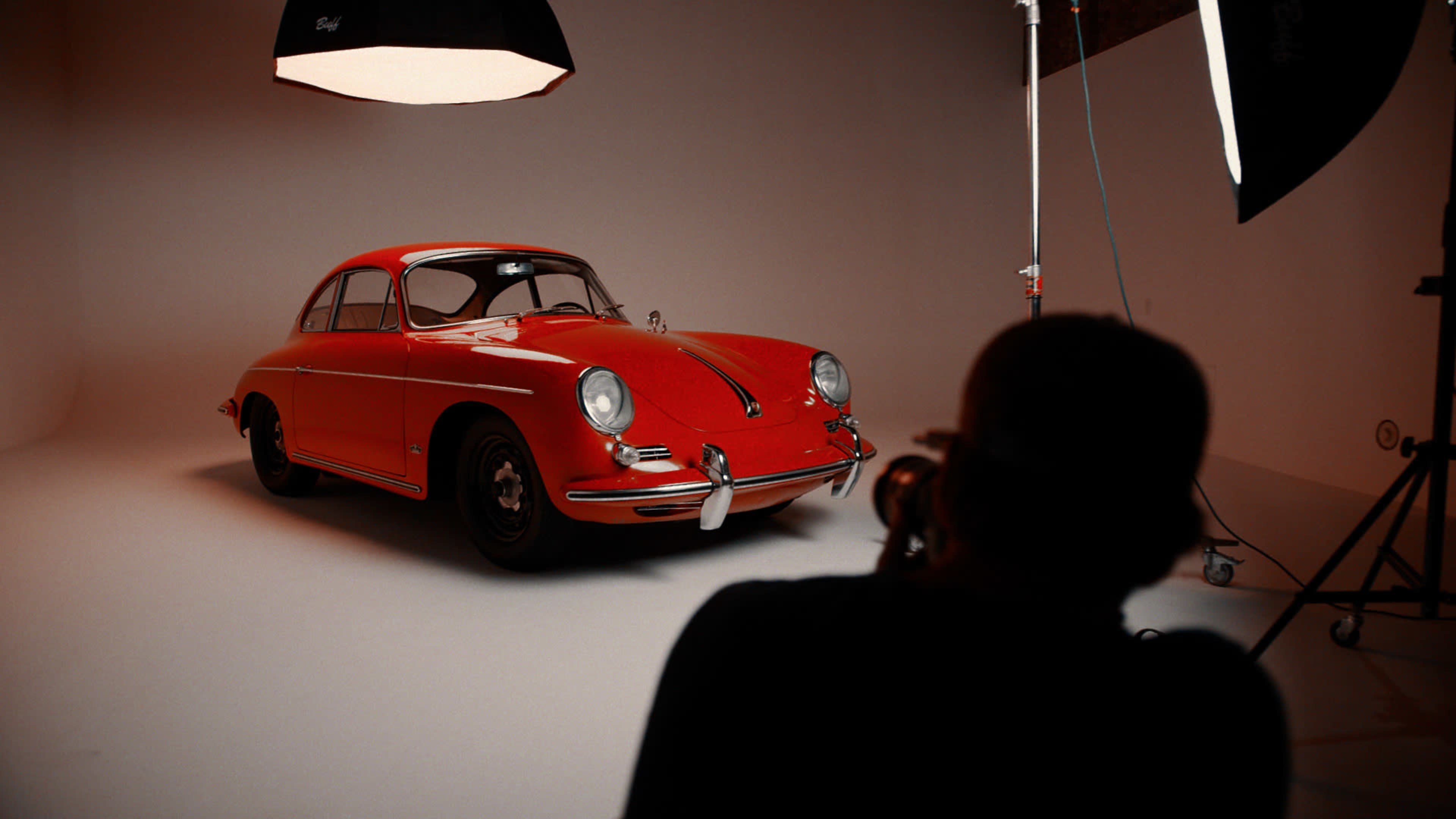 A photographer captures a red vintage car under studio lighting against a white backdrop.