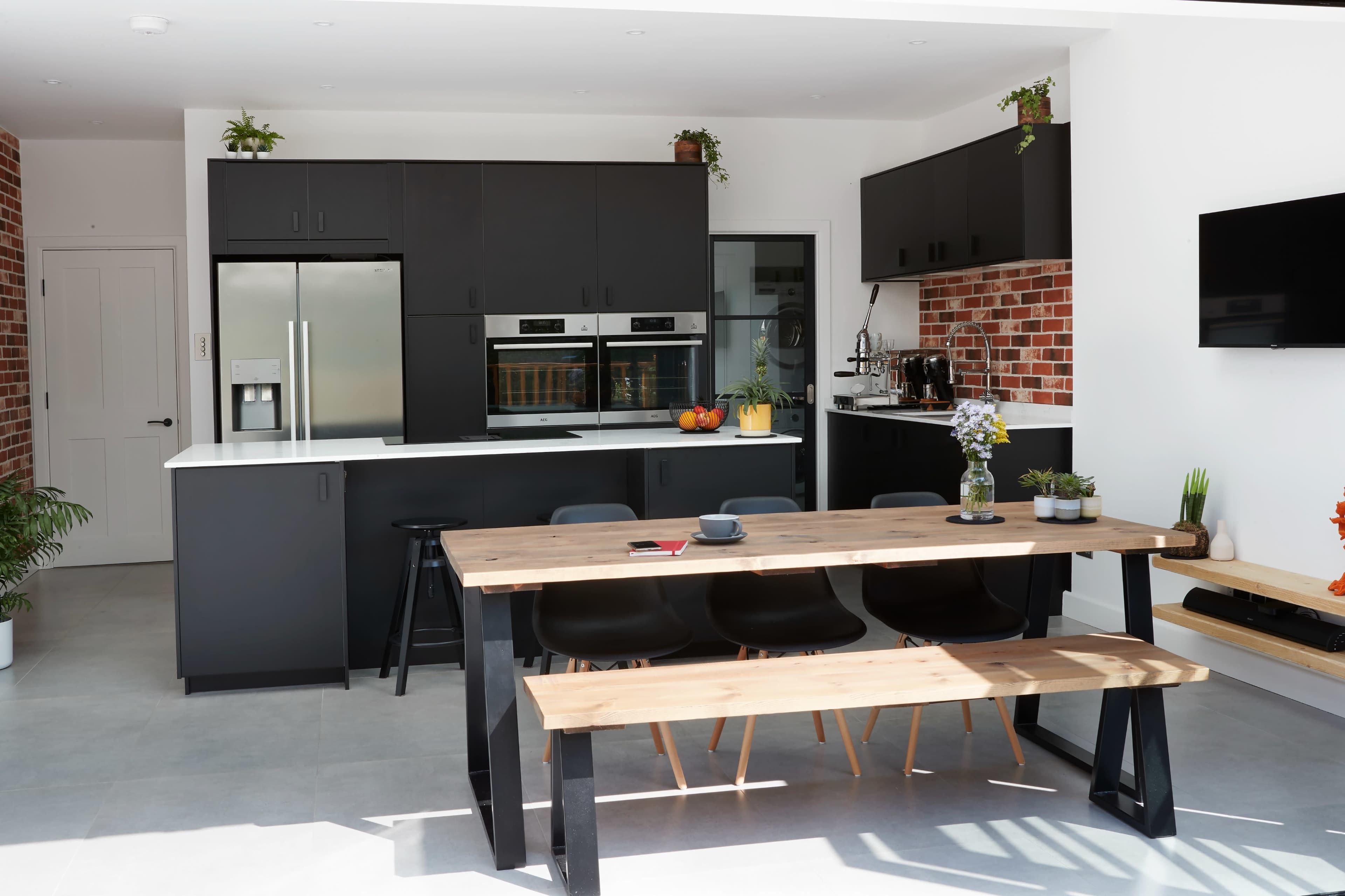 A modern kitchen features black cabinetry, stainless steel appliances, and a wooden dining table with black chairs.