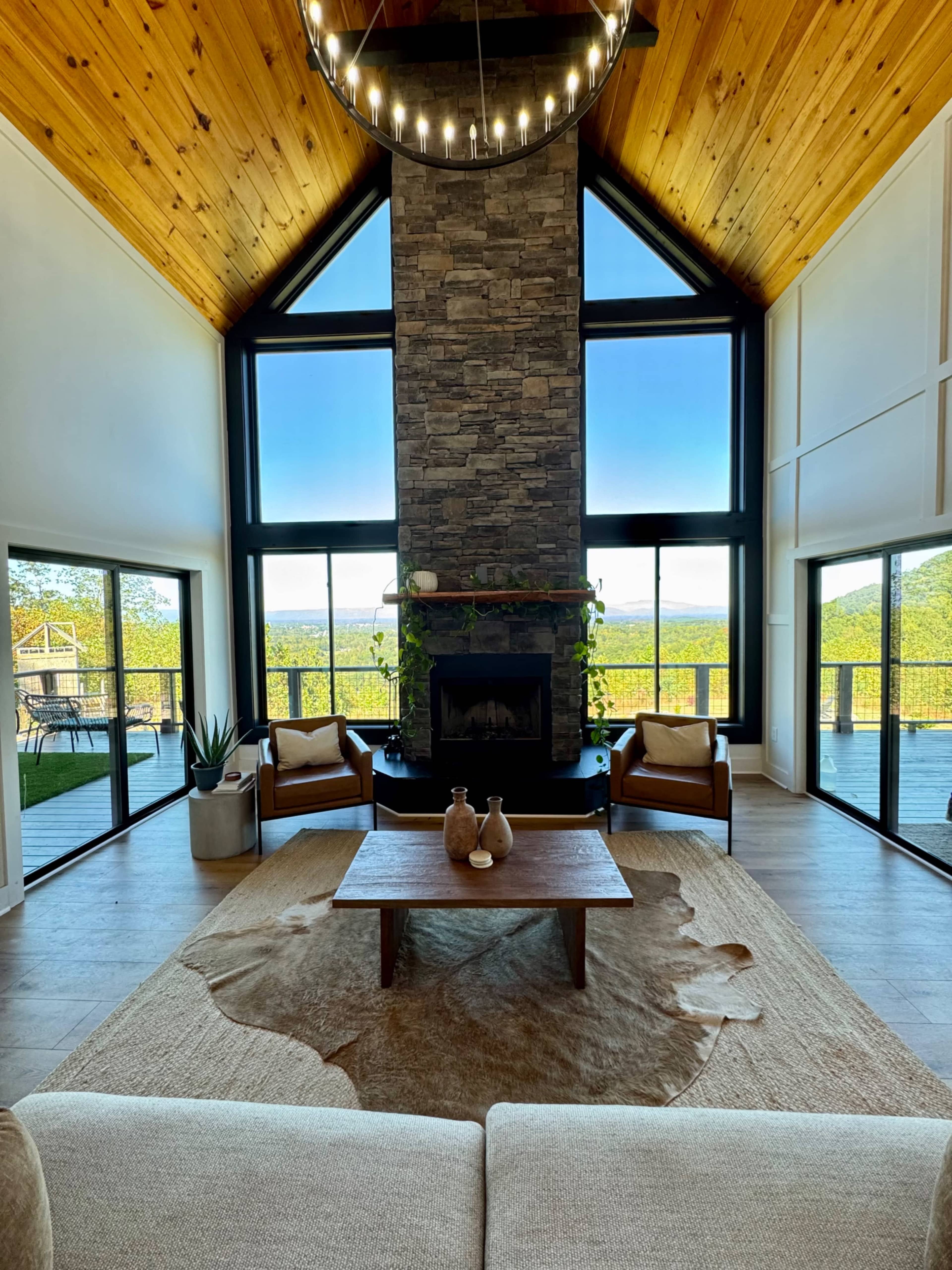 A spacious living room features a stone fireplace, large windows with a scenic view, and modern furnishings on a natural fiber rug.