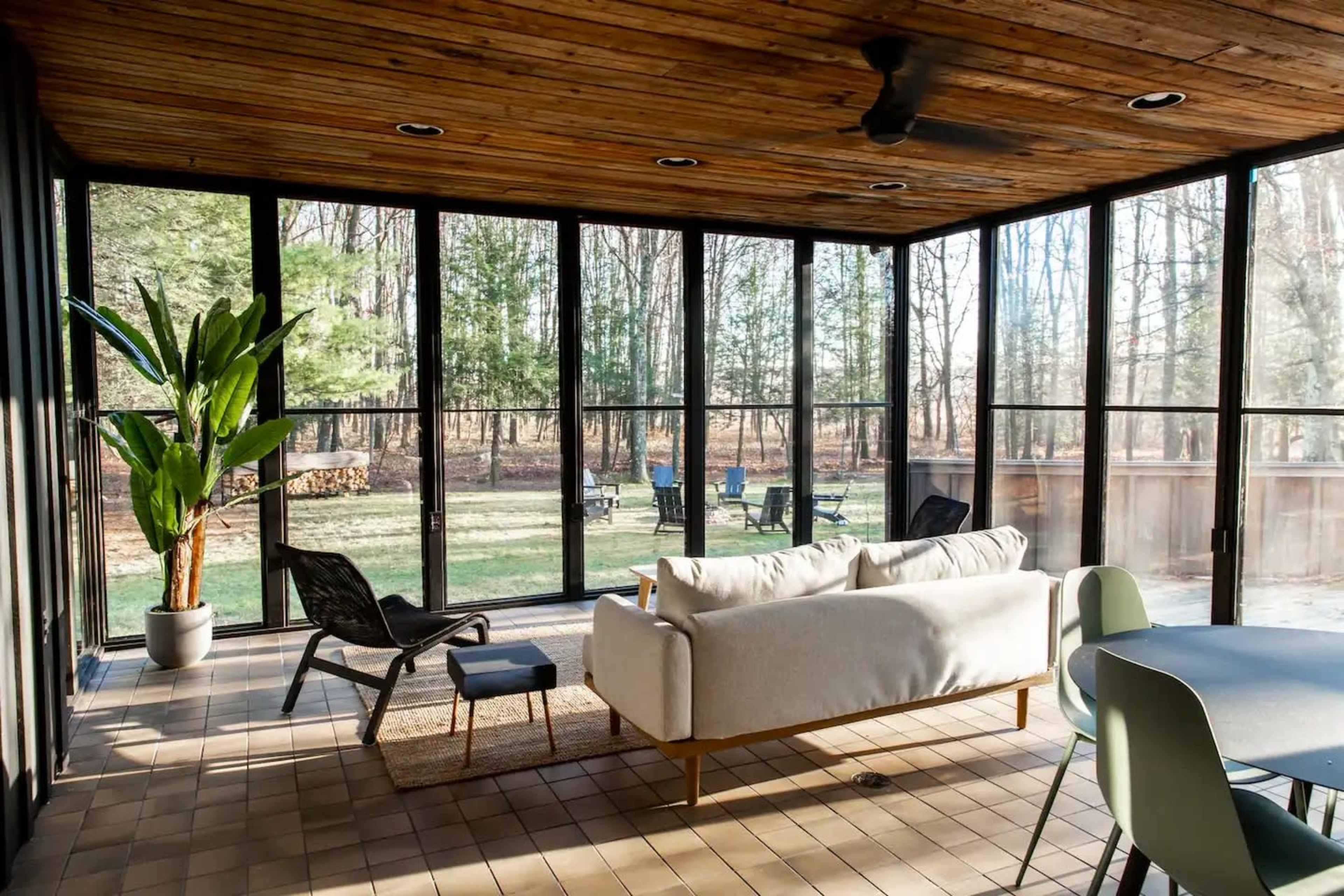 A screened-in porch features a sofa, chairs, and a view of a grassy yard with trees in the background.