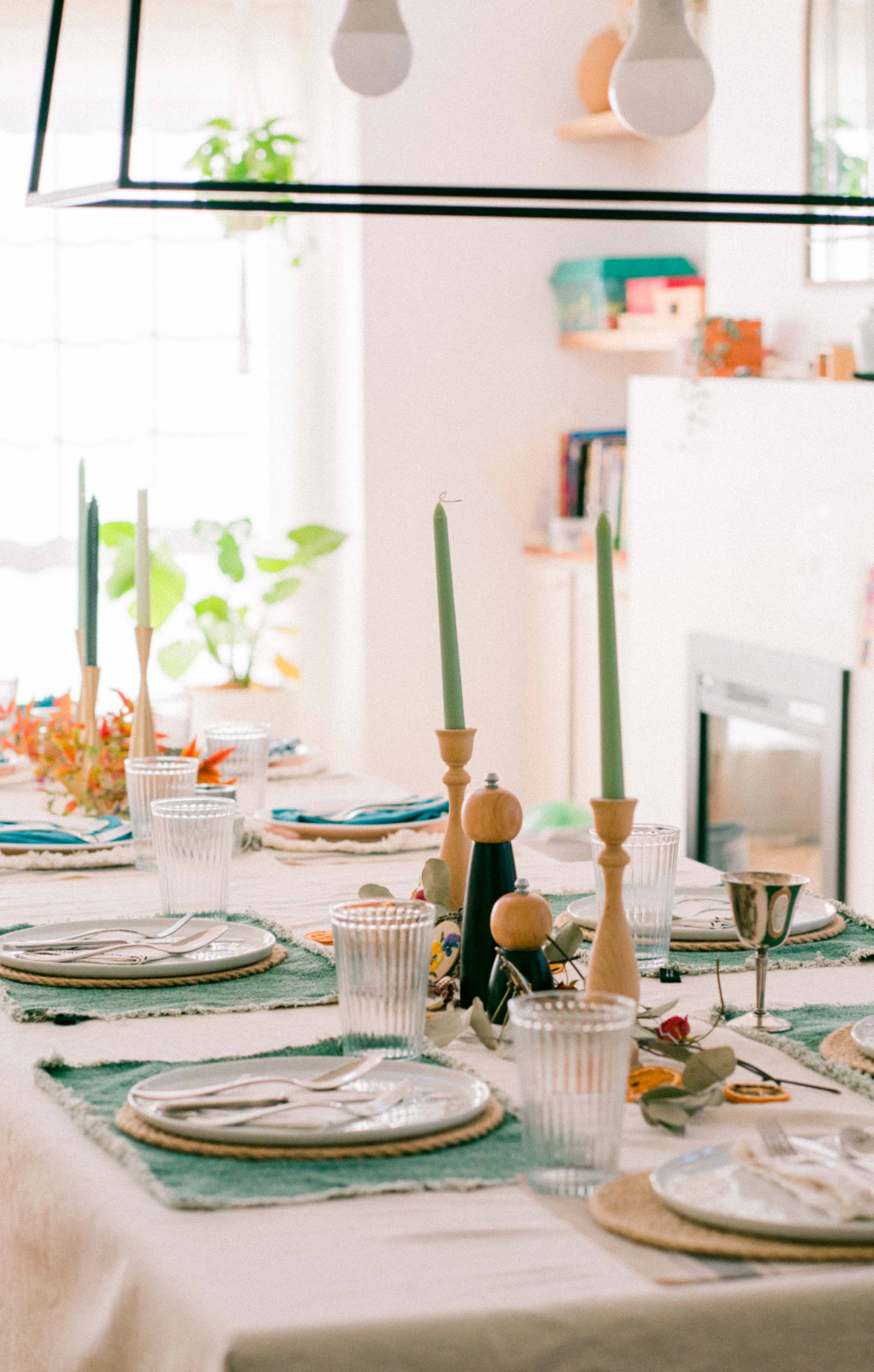 A dining table is set with plates, glasses, cutlery, and decorative candles in a bright, modern room.