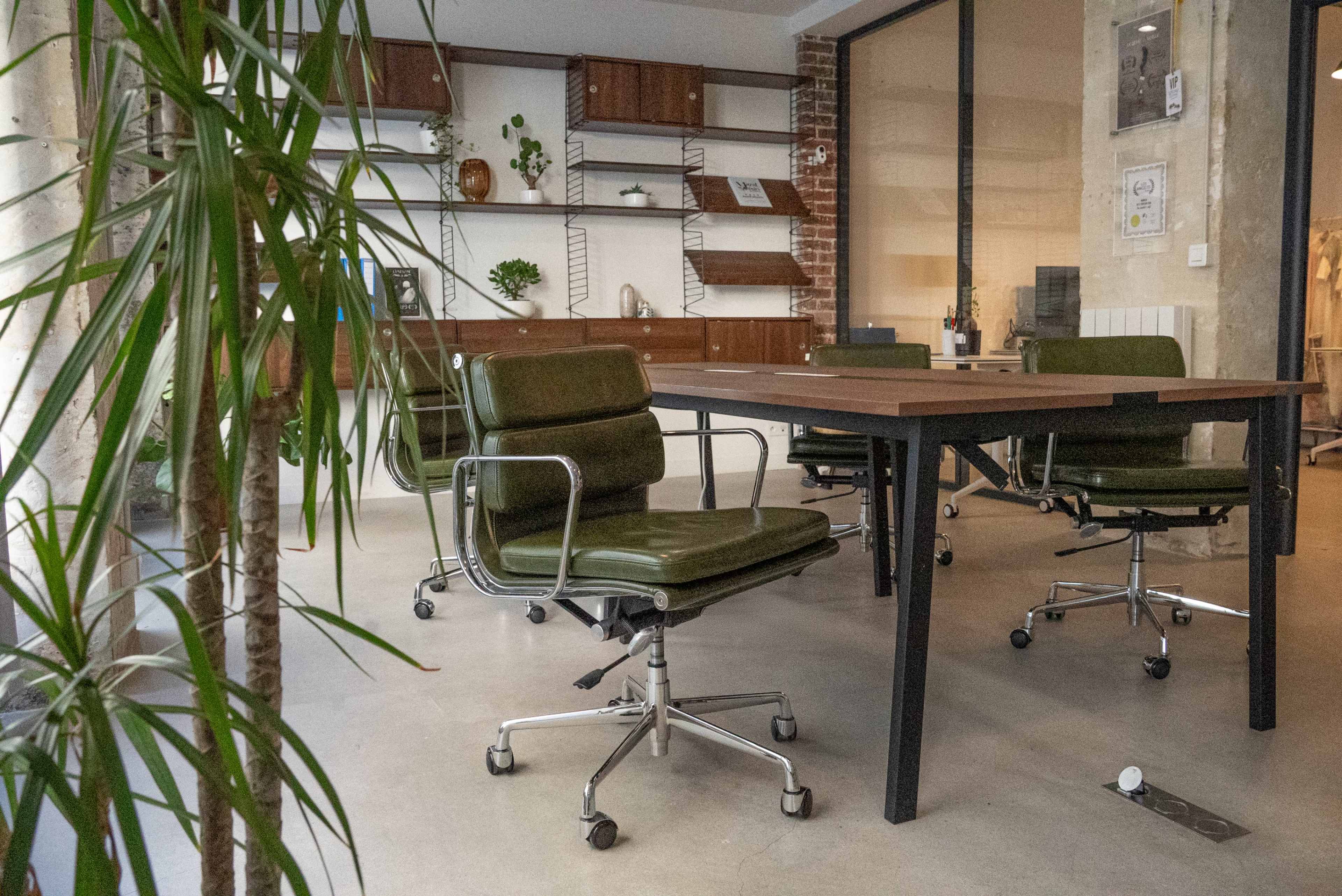 The image shows a modern office space with green swivel chairs surrounding a wooden table, accompanied by shelves with decorative items and plants.