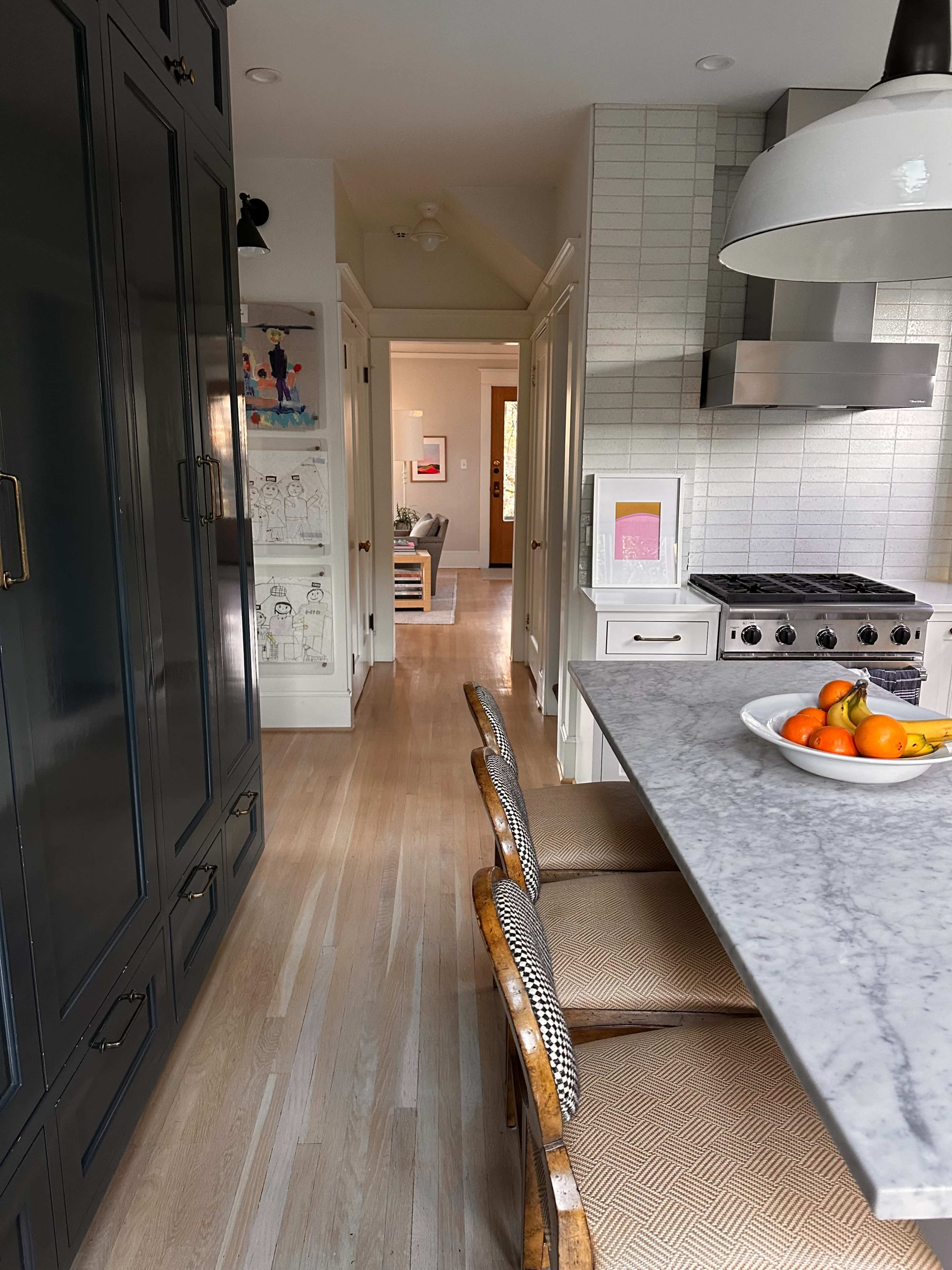 A hallway leads from a modern kitchen with a marble countertop and stainless steel appliances to a bright, inviting living space.