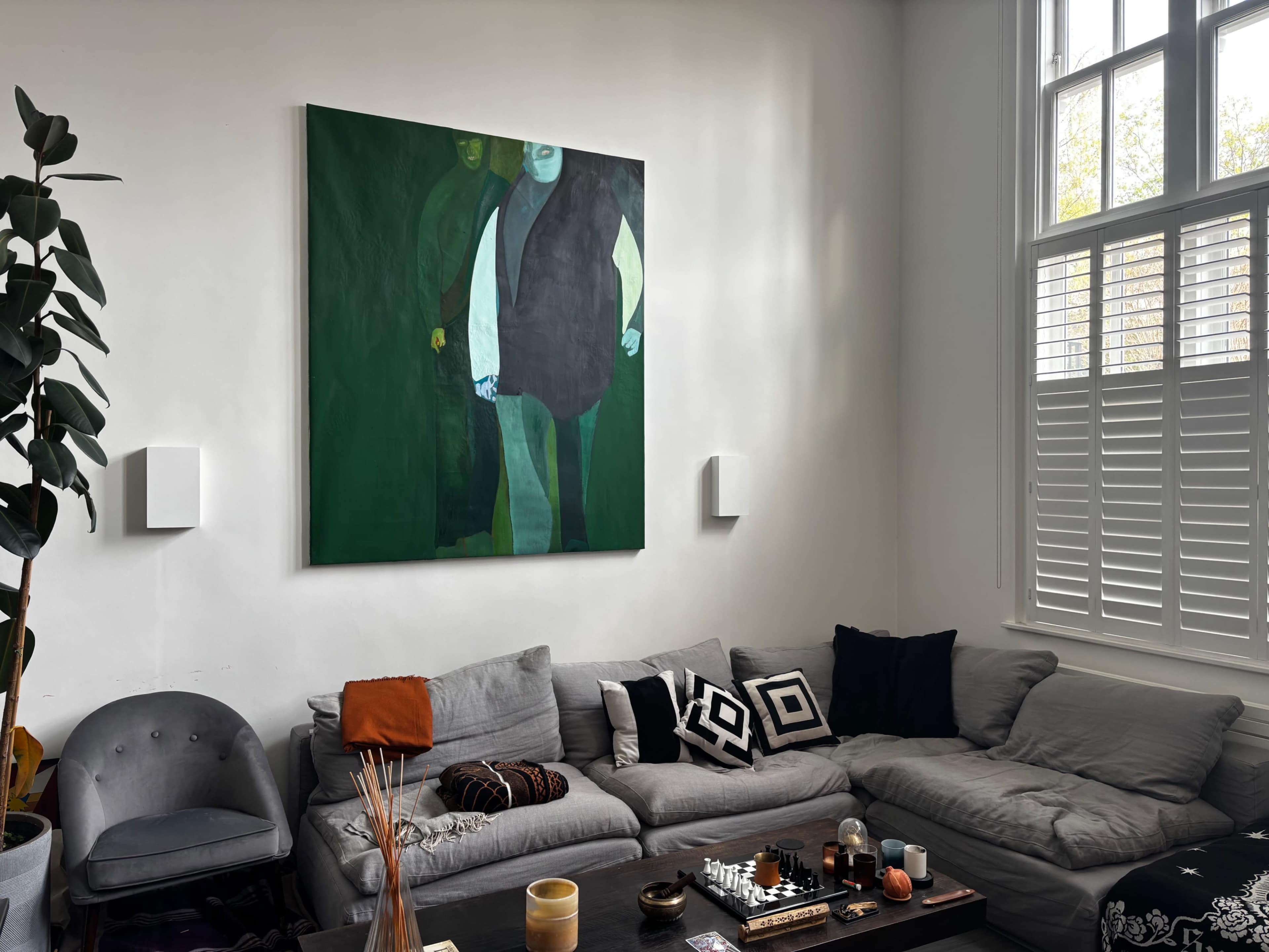 The image shows a living room with a grey sectional sofa, decorative cushions, a coffee table with various items, and a large abstract painting on the wall.