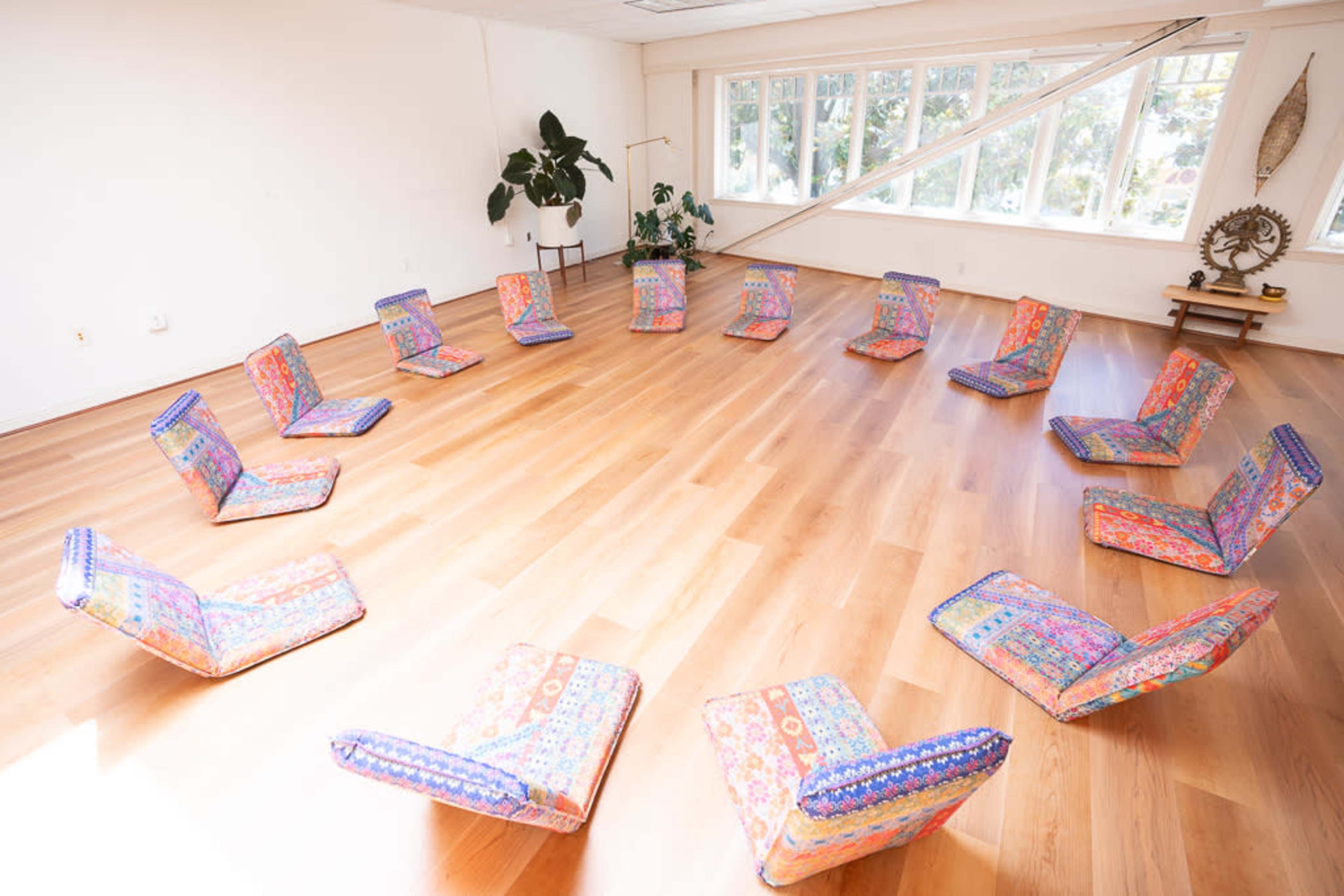 A circular arrangement of cushioned chairs in a spacious room with large windows and wooden flooring.