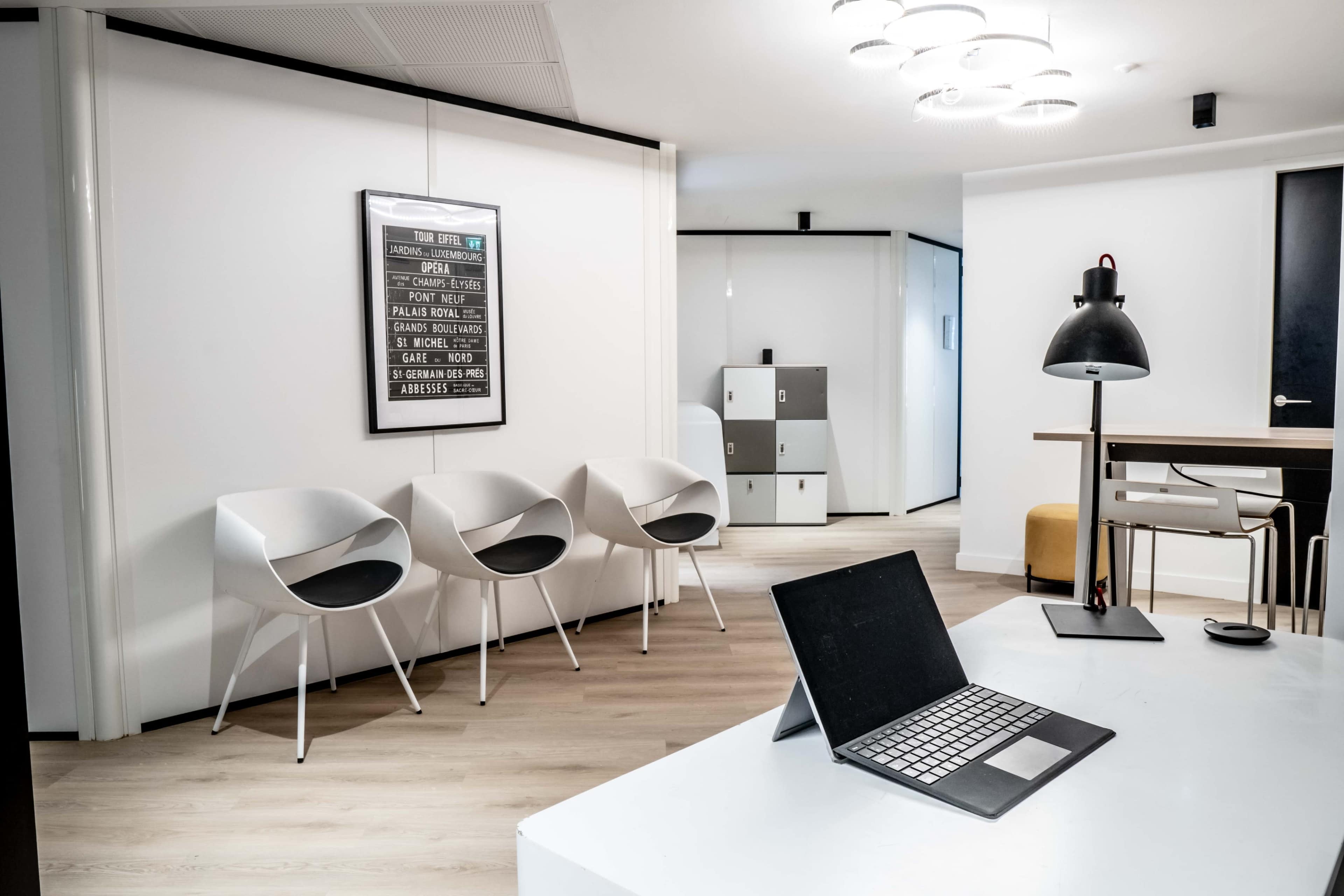 The image shows a modern office space featuring three white chairs, a desk with a laptop, and a decorative wall-mounted poster.