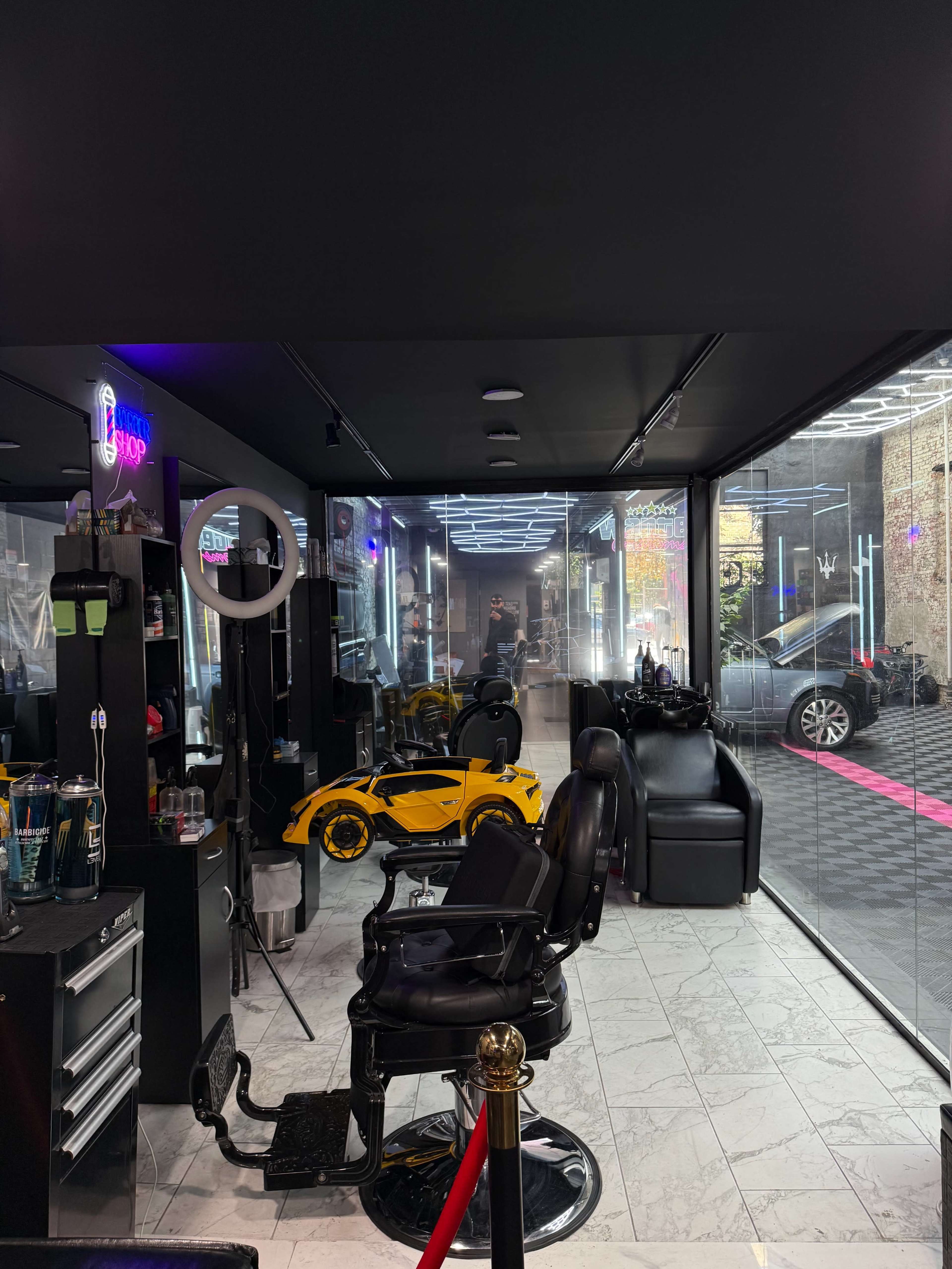 The image shows a modern hair salon featuring black styling chairs, brightly lit mirrors, and a toy car positioned near the entrance.