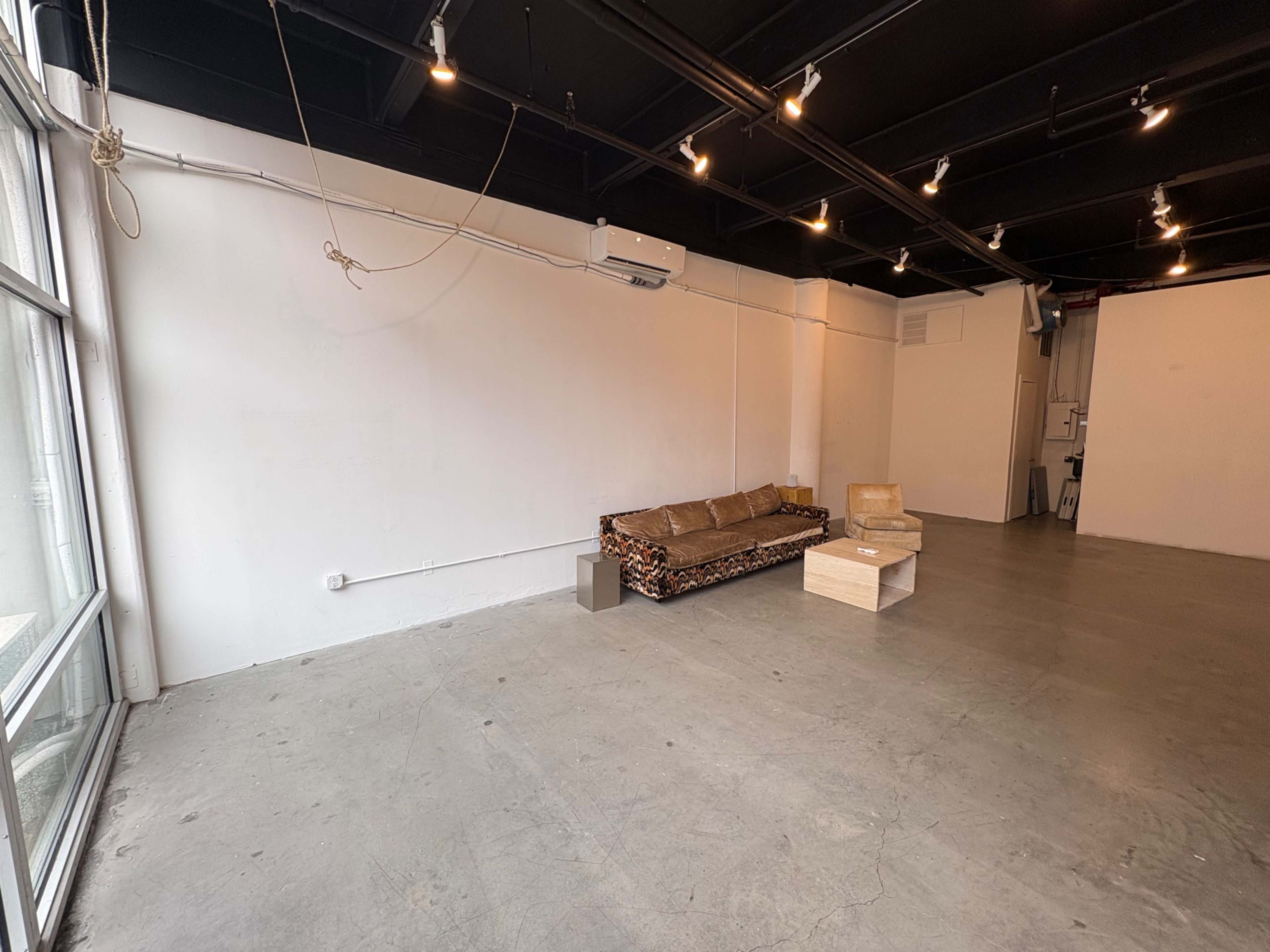 The image shows an empty industrial-style space with polished concrete flooring, a patterned couch, and a minimalist coffee table.