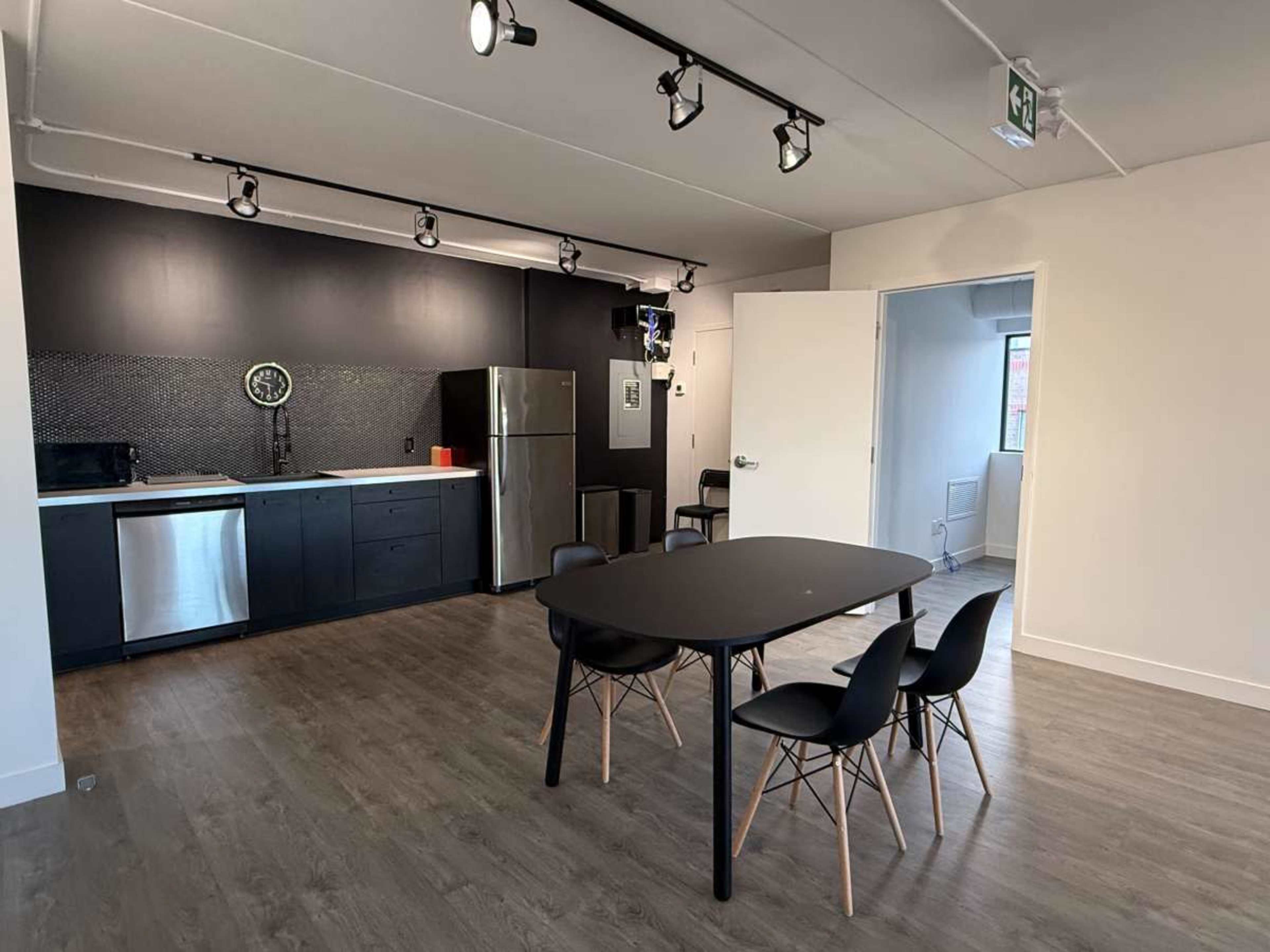 The image shows a modern kitchen and dining area with a black and stainless steel color scheme, featuring a dining table with four chairs and a refrigerator.