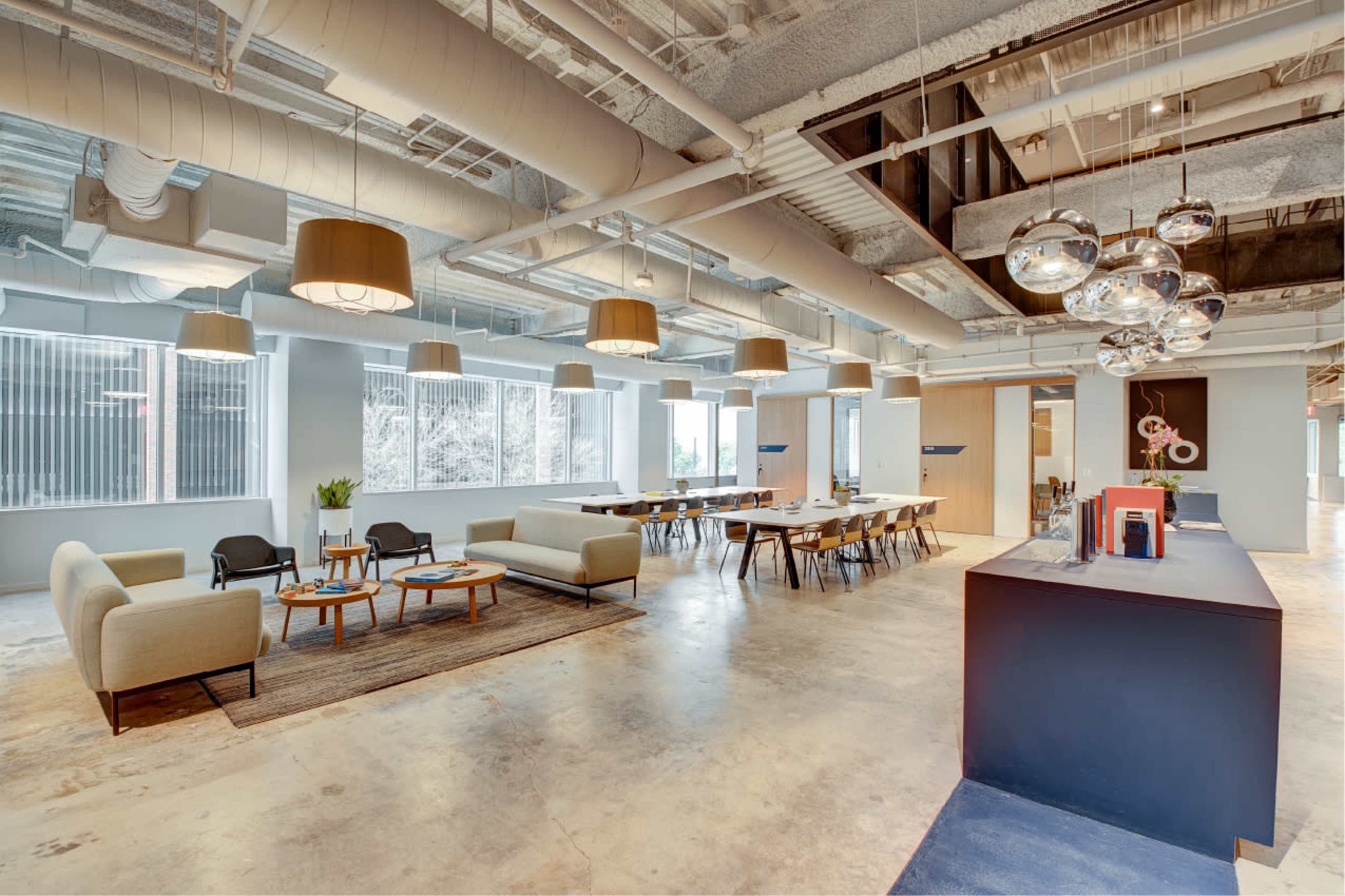 A modern office interior with seating areas, a dining space, and pendant lighting.