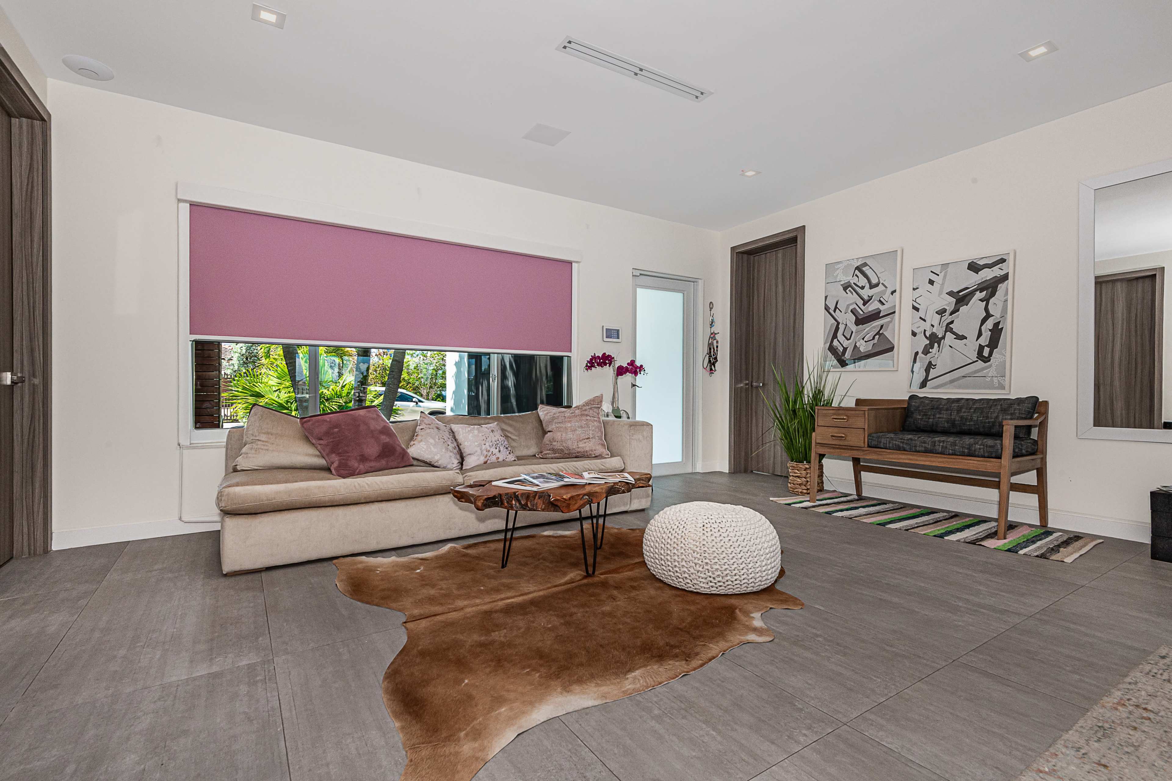 The image shows a modern living room featuring a beige couch, a decorative rug, a wooden coffee table, and two framed artworks on the walls.