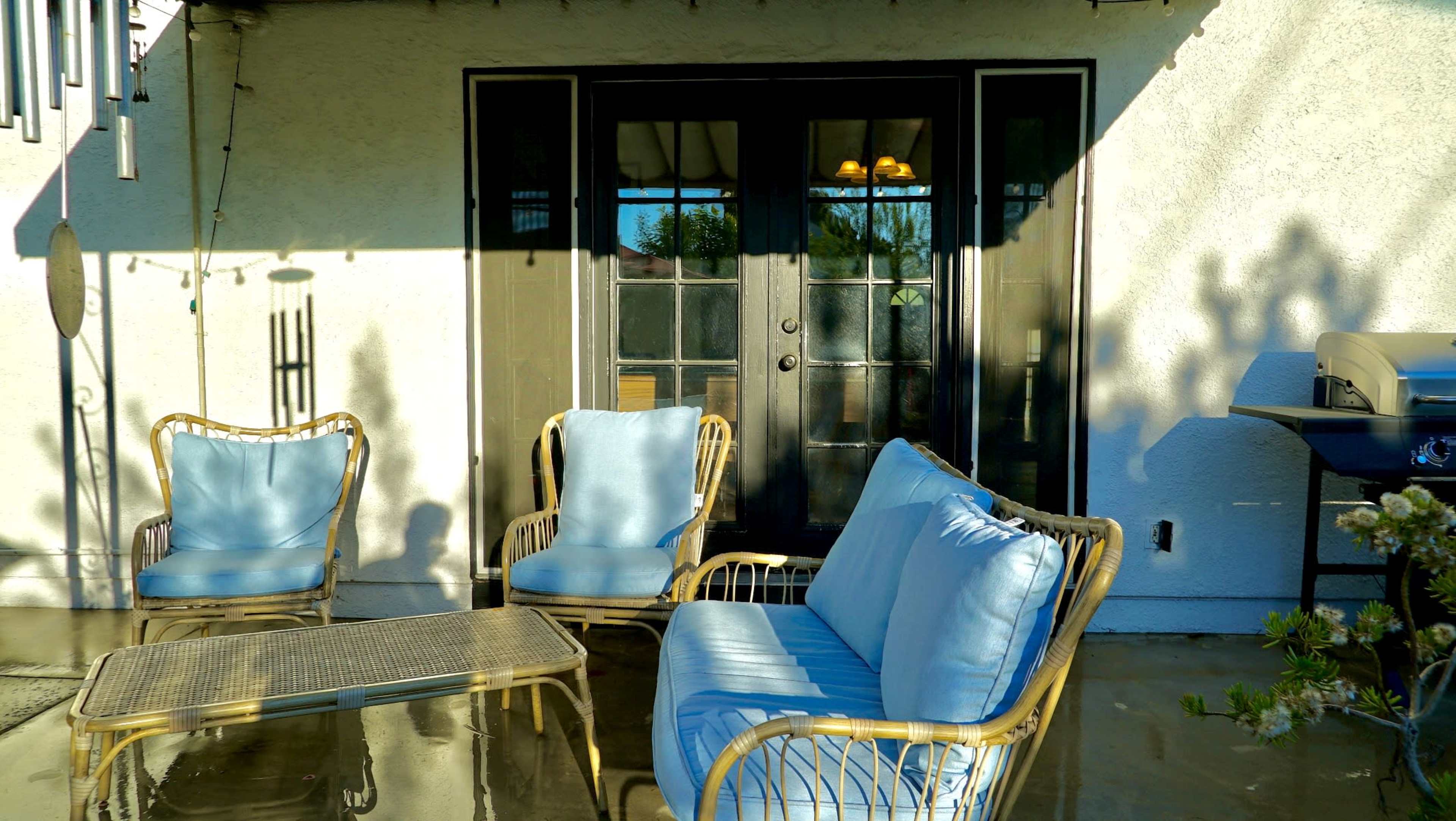 A set of blue cushioned wicker chairs and a coffee table are positioned on a patio in front of a set of double glass doors.