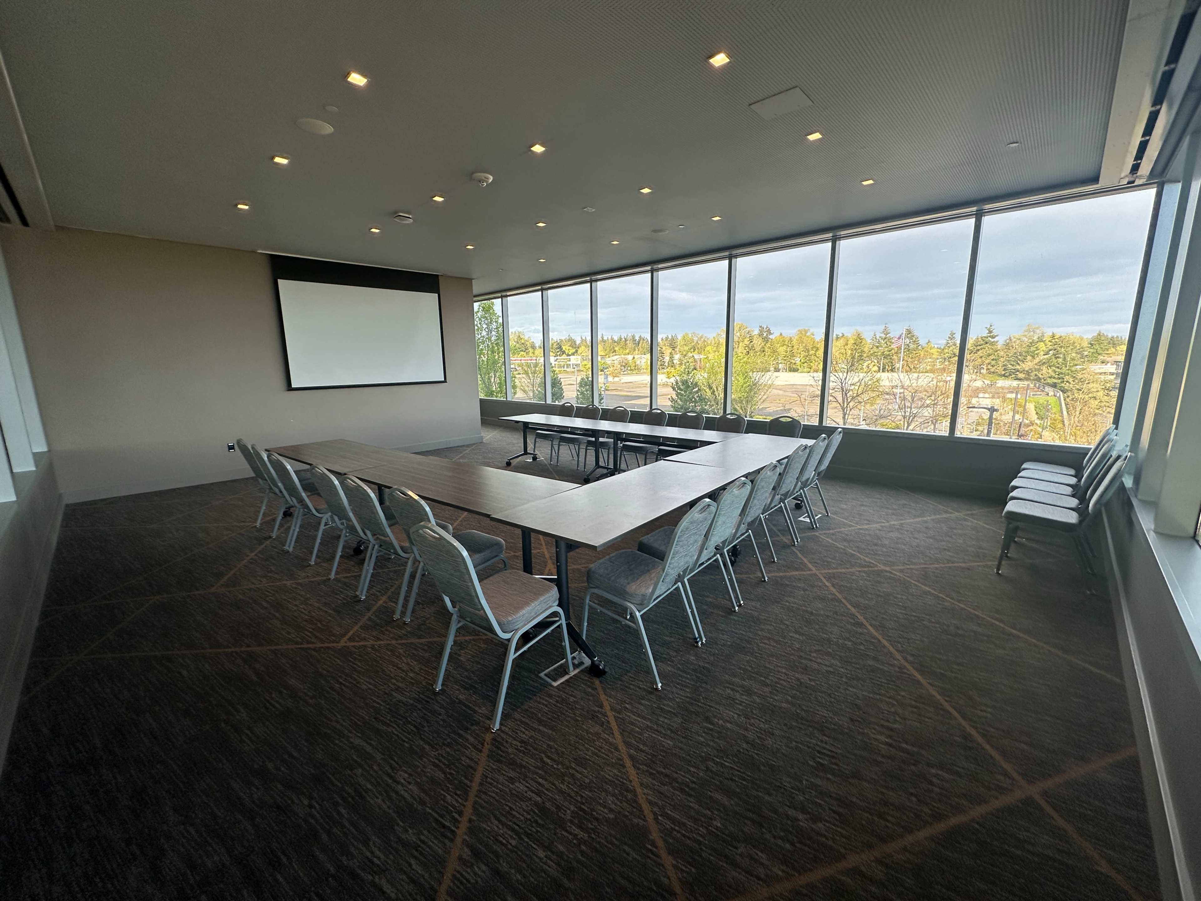A large conference room features a long table surrounded by chairs, with windows offering a view of the outdoors.
