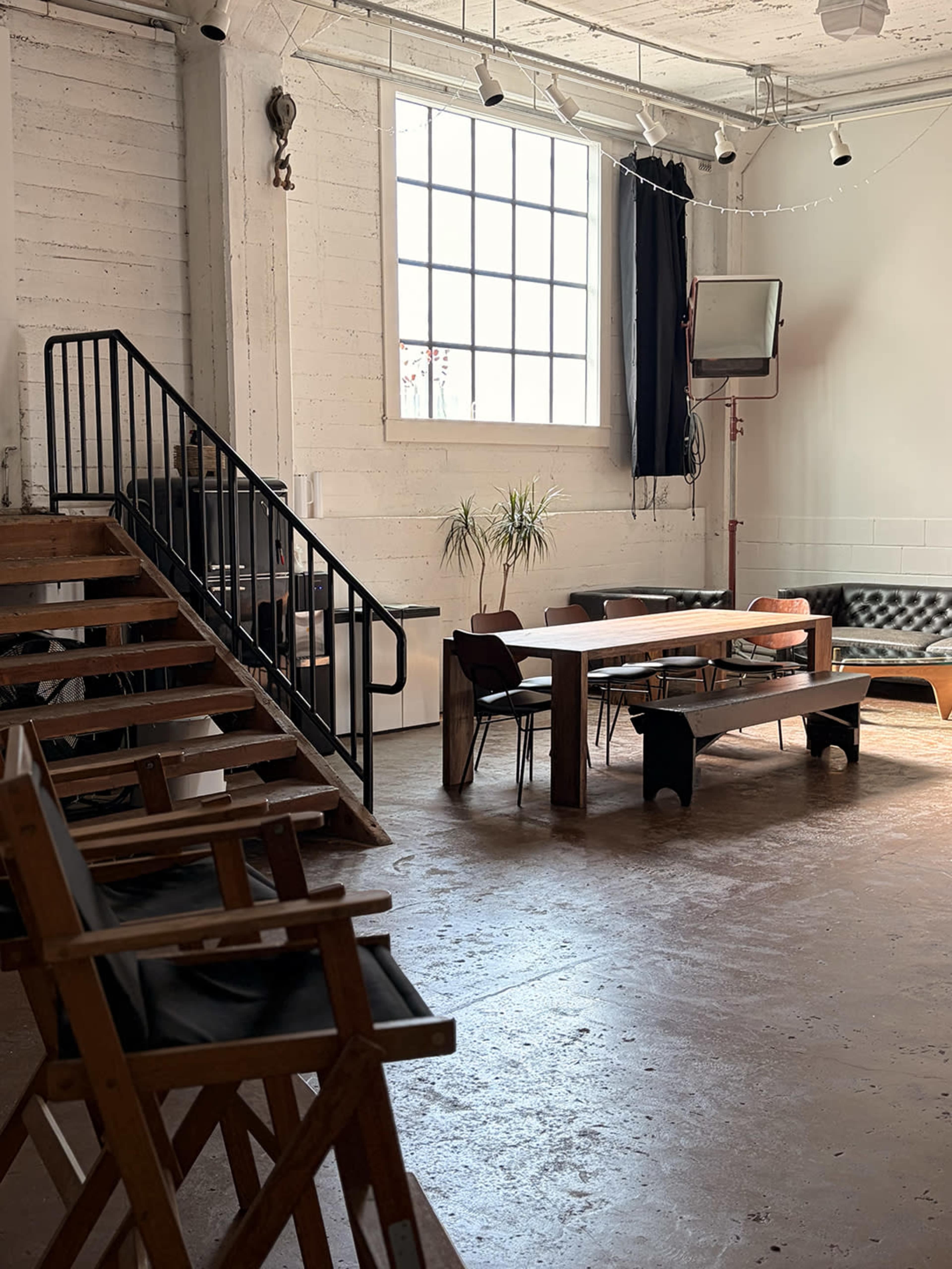 The image shows a spacious, well-lit interior with a staircase, a large dining table, and several seating areas.
