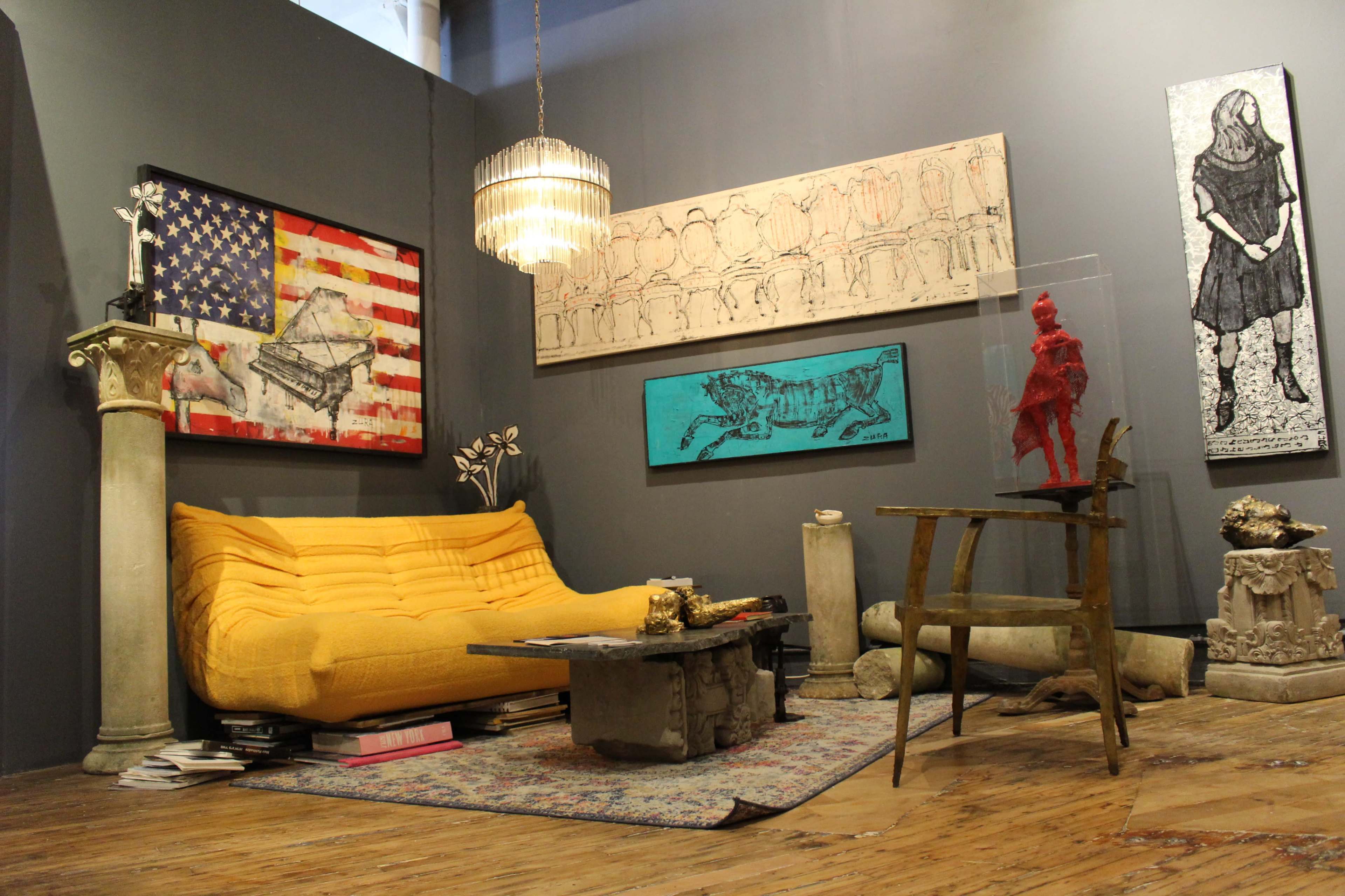 The image depicts a stylish interior space featuring a yellow sofa, two large artworks on the wall, a small table with decorative items, and various architectural elements incorporated into the decor.
