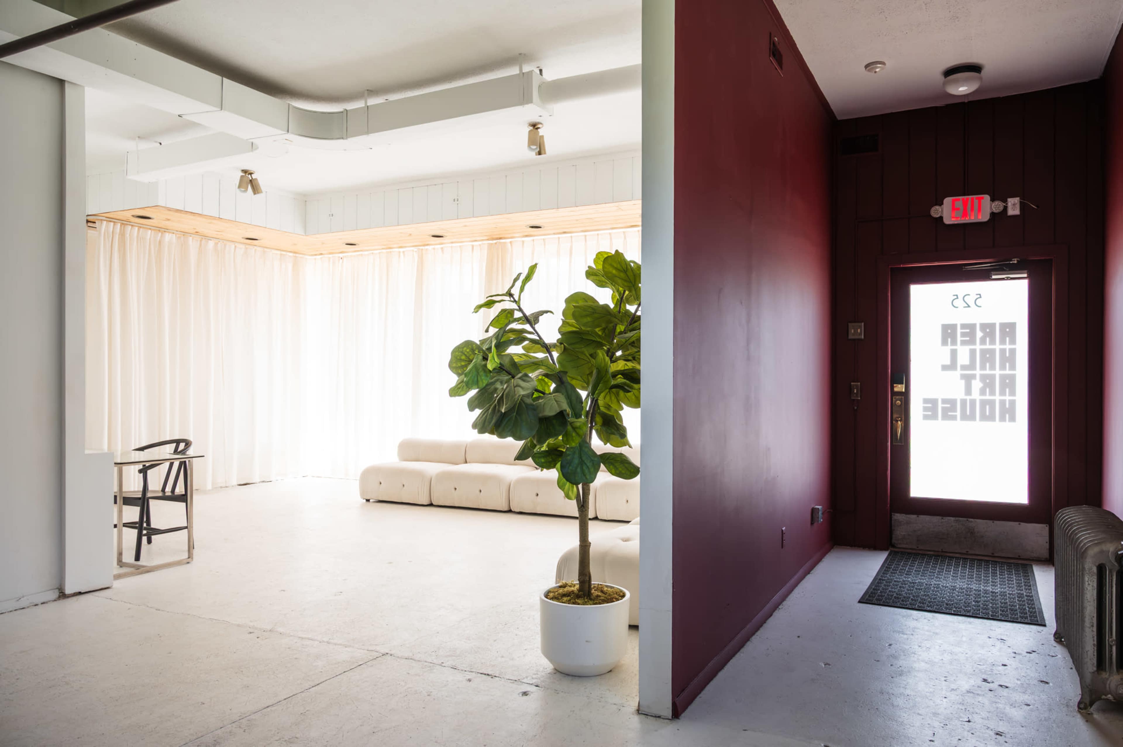 The image shows a modern interior space with a white sofa, a small table, and a large curtain, alongside a red wall with a door labeled "REAR HALL ART HOUSE."
