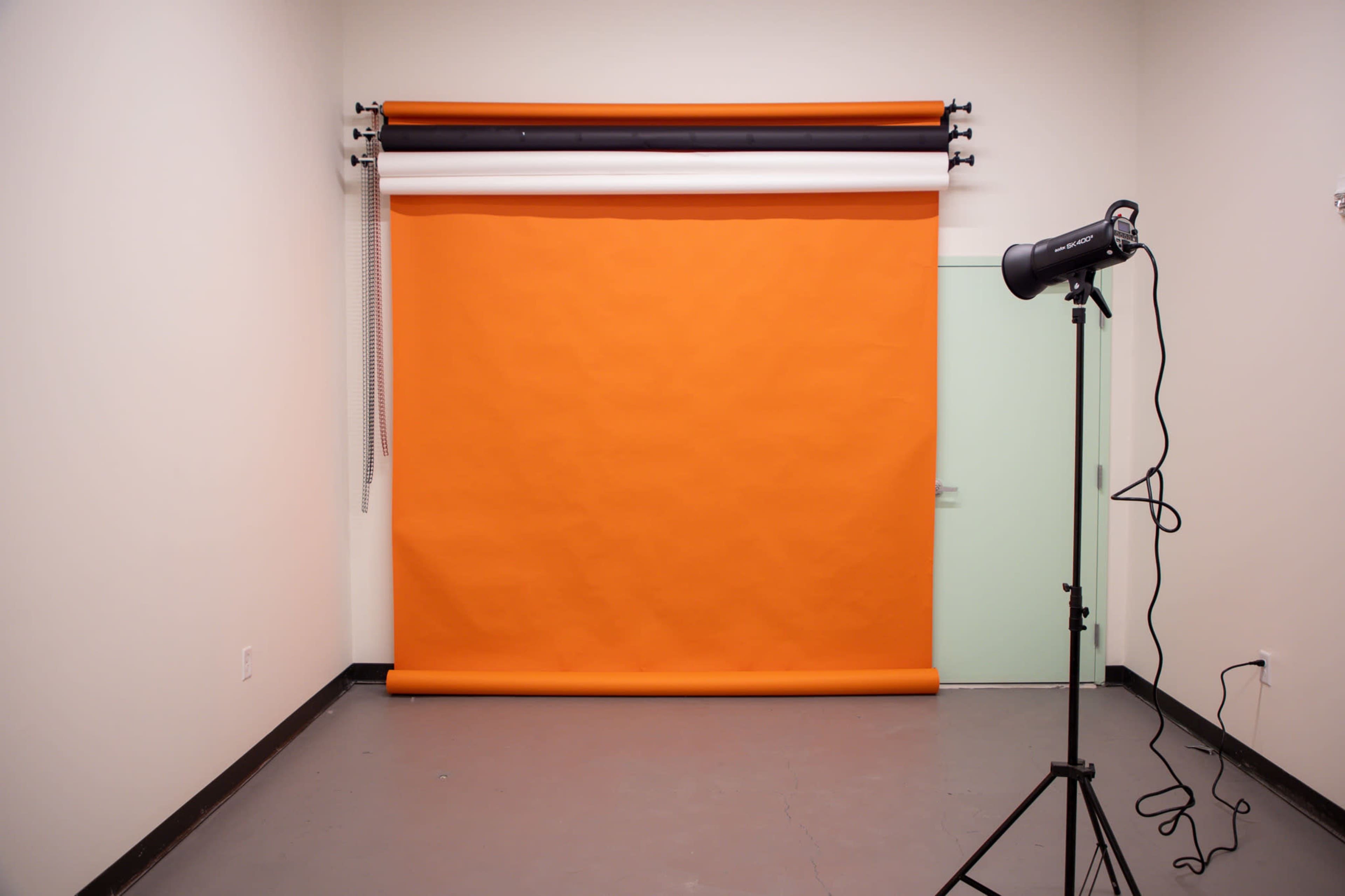 A photography studio with an orange backdrop rolled down and a light stand positioned next to it.