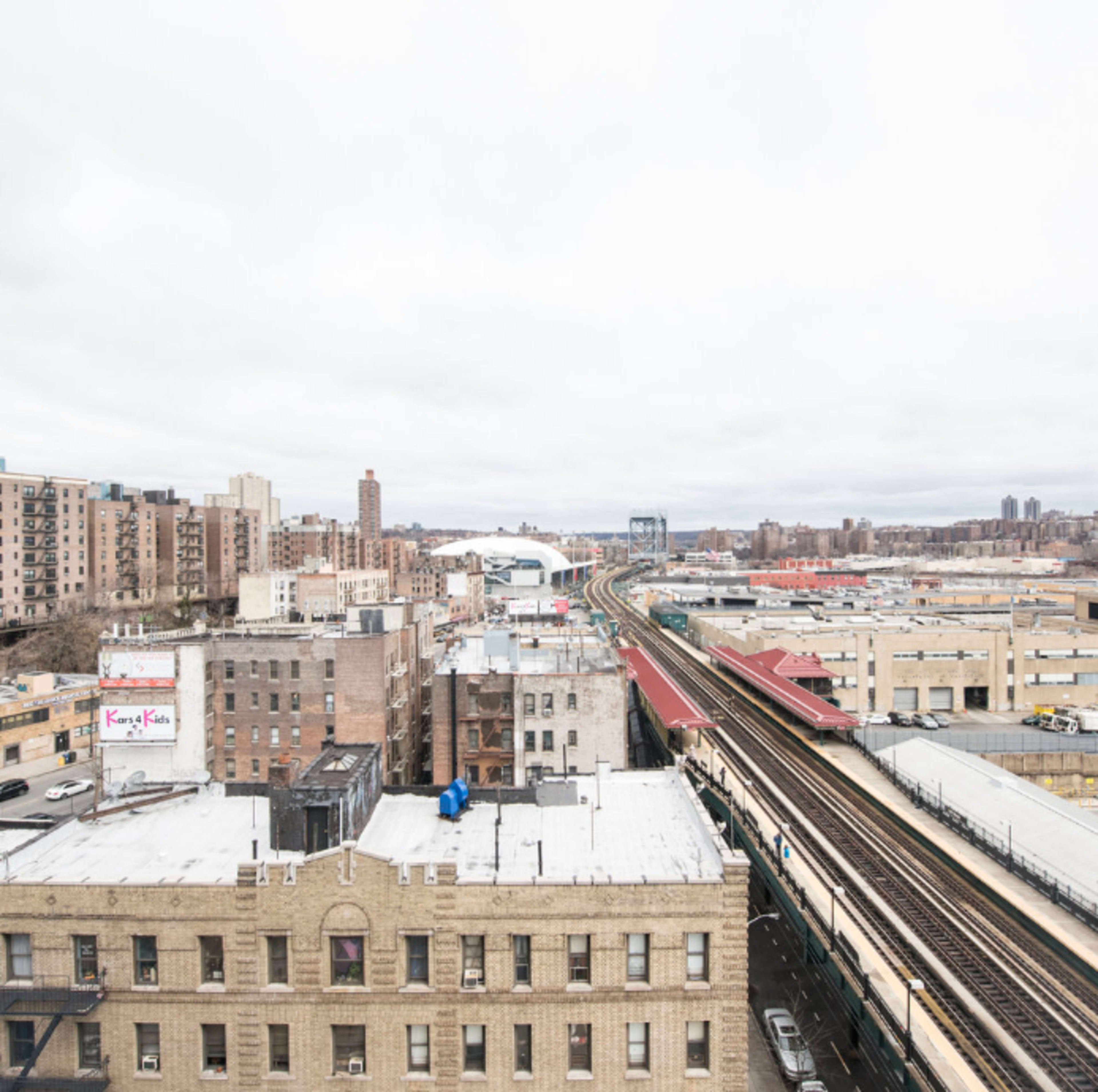 A view of a cityscape featuring buildings, elevated train tracks, and a cloudy sky.