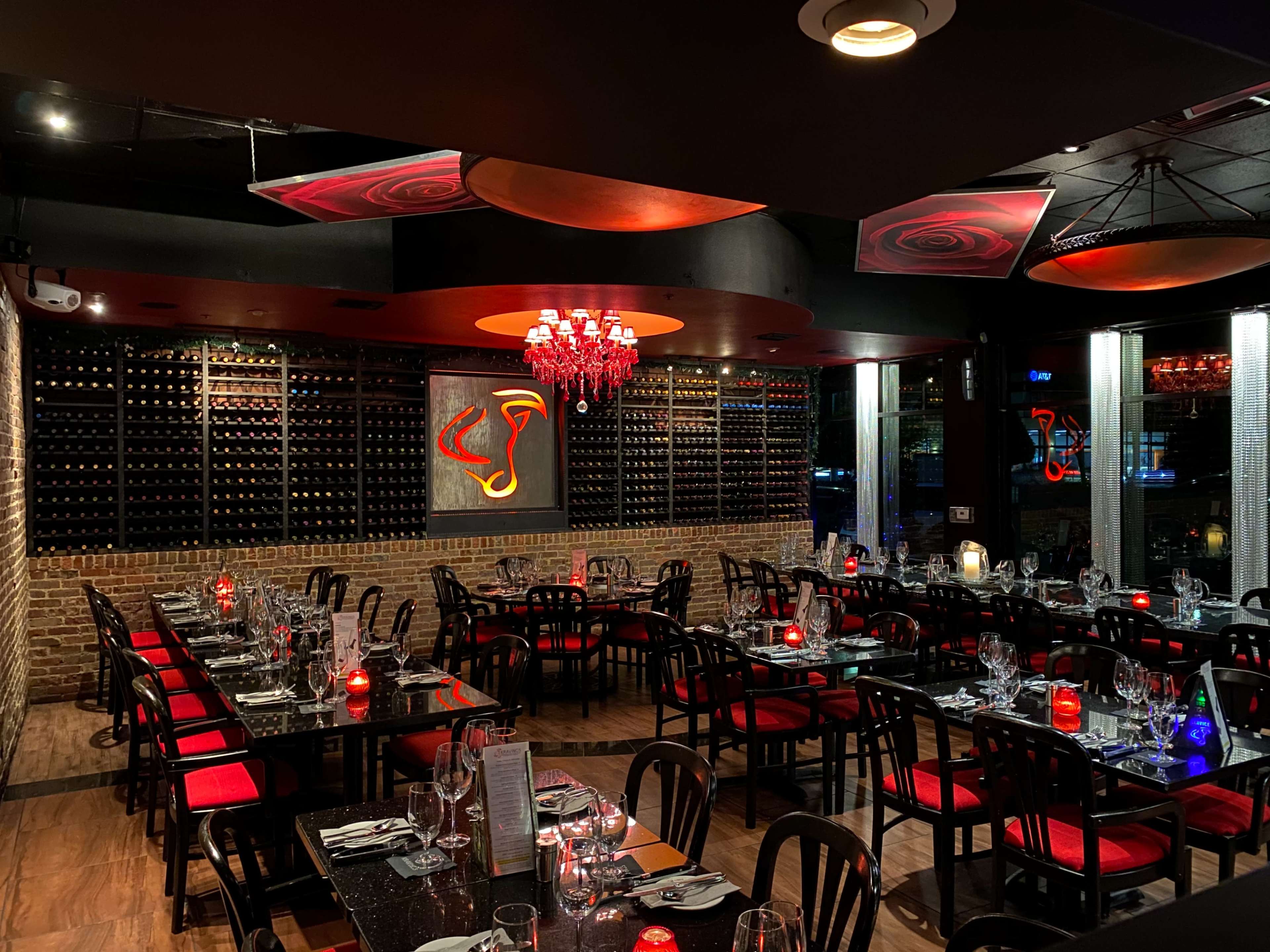The image shows a dimly lit restaurant with dark furniture, red accents, and a wine rack displayed on the back wall.