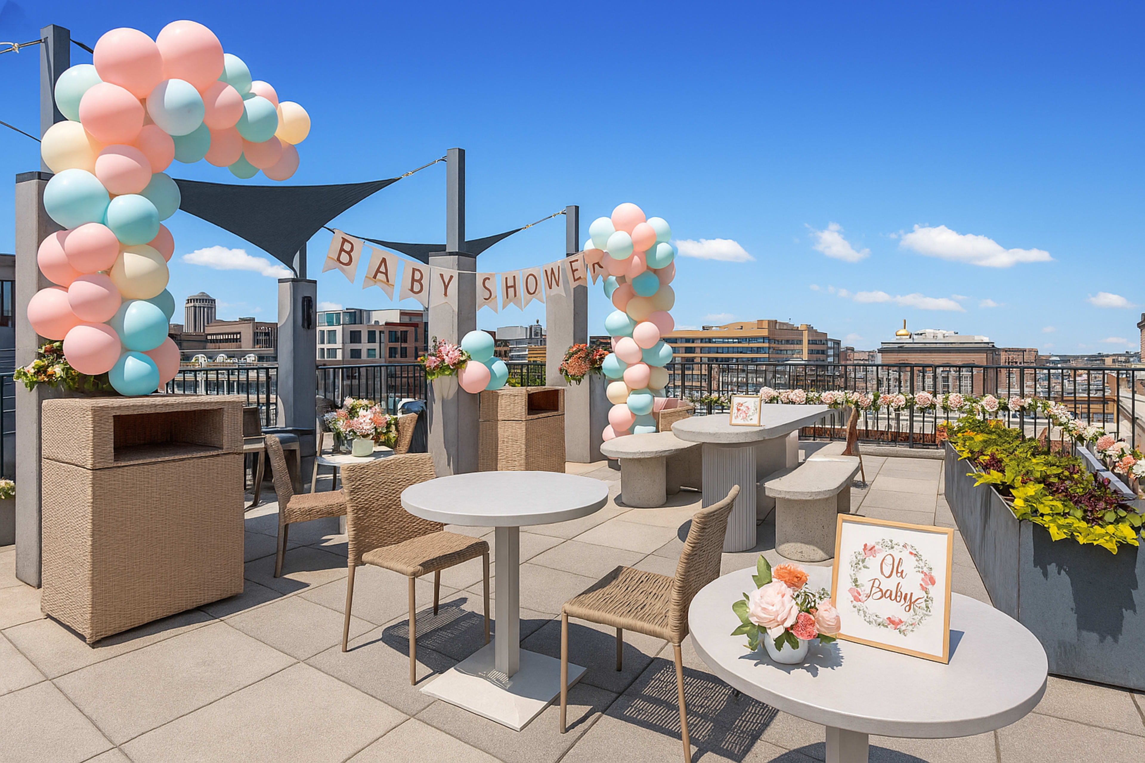 The image shows a decorated rooftop area set up for a baby shower, featuring pastel balloon arches, tables, and floral arrangements.