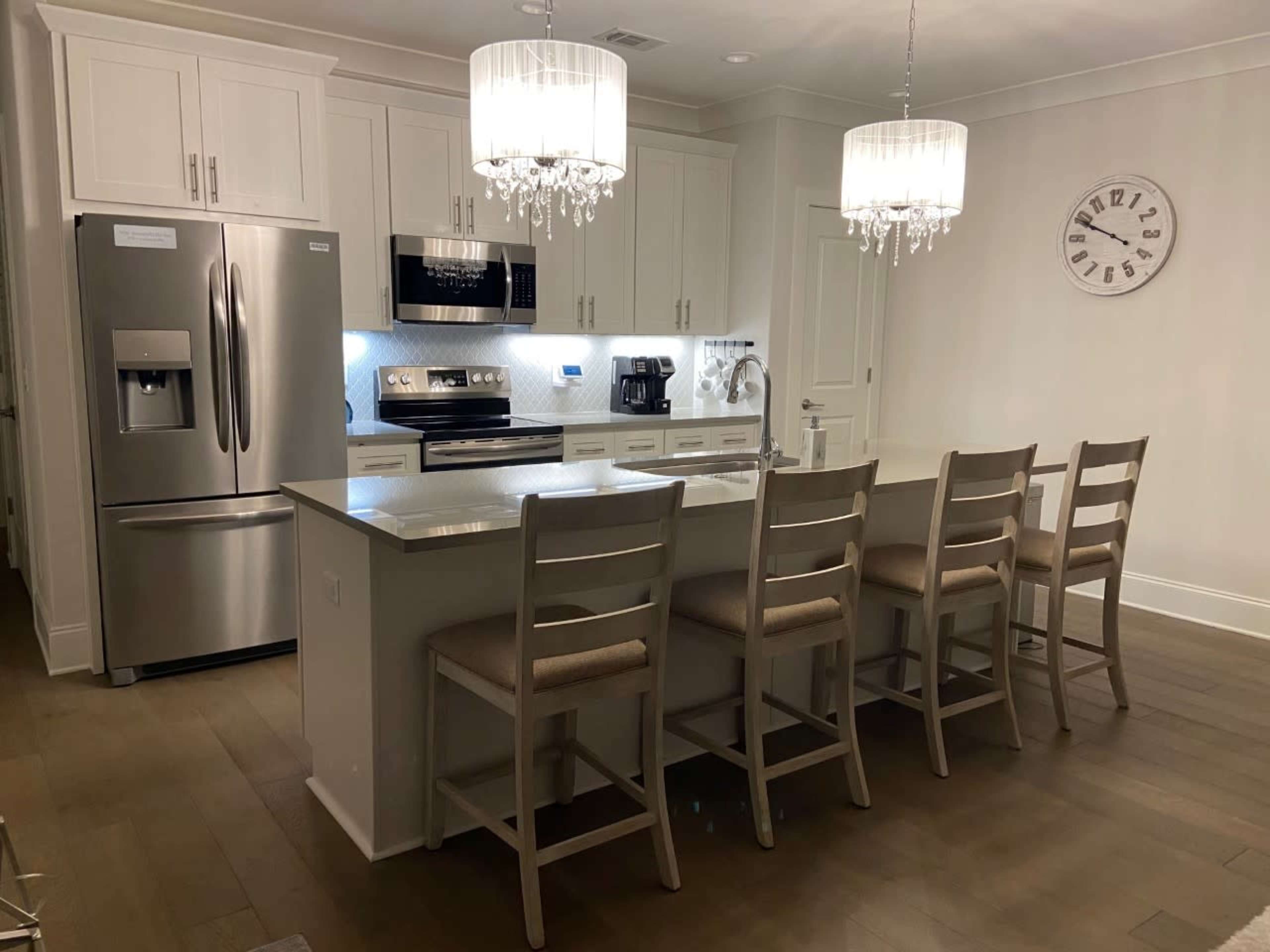 A modern kitchen with white cabinetry, stainless steel appliances, and a large island with seating for six.