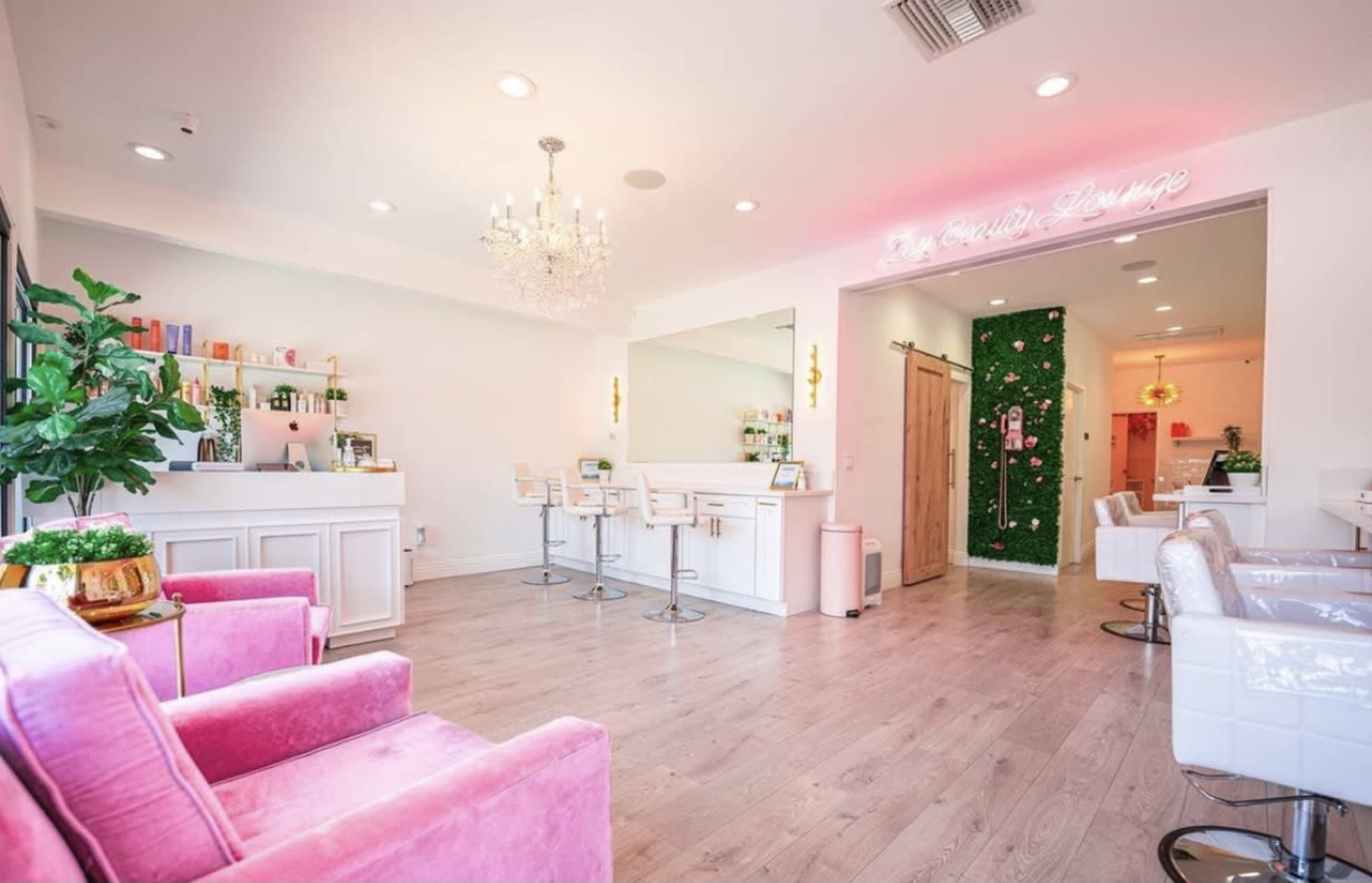 A brightly lit beauty salon features pink furniture, a reception area with a bar, and a decorative green wall.