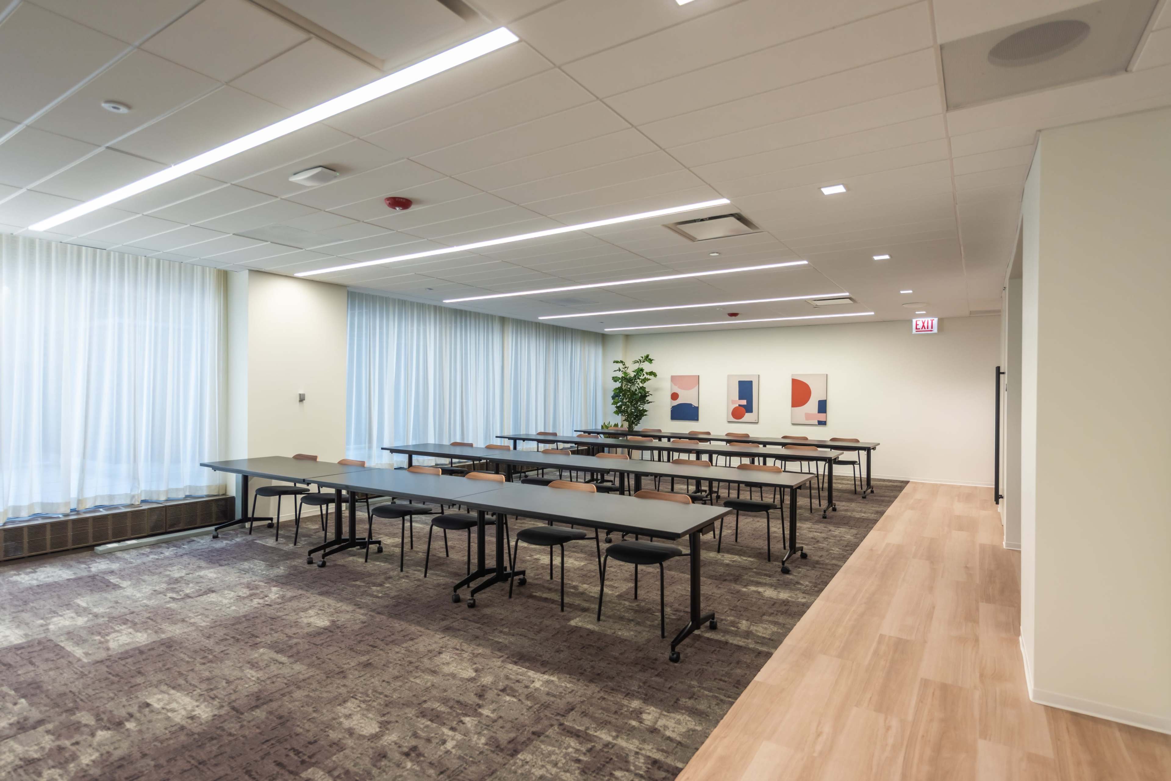 The image shows a bright, modern conference room with several rows of tables and artwork on the walls.