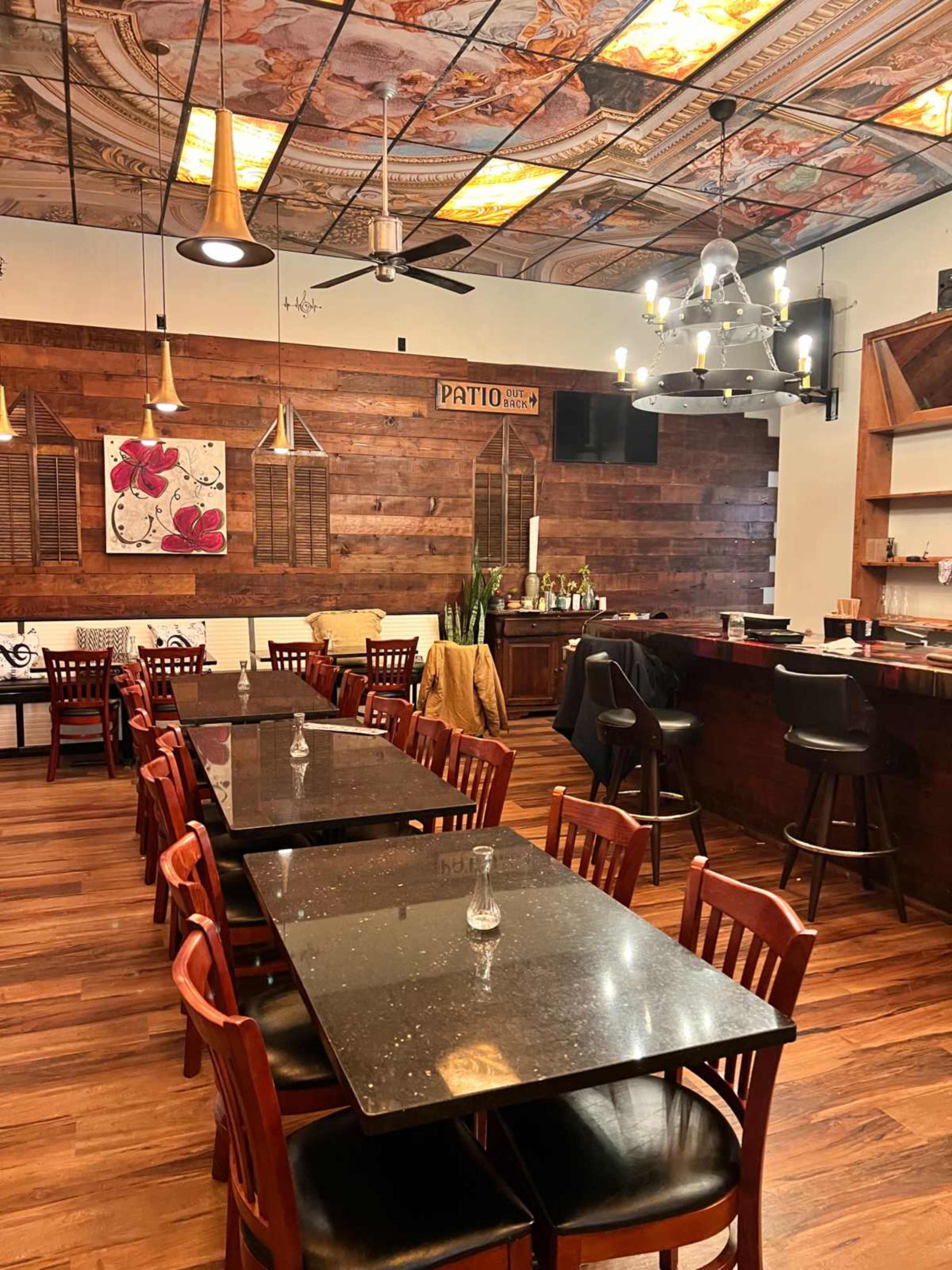 The image shows a dining area in a restaurant featuring wooden walls, dark tables, red chairs, and decorative ceiling lights.