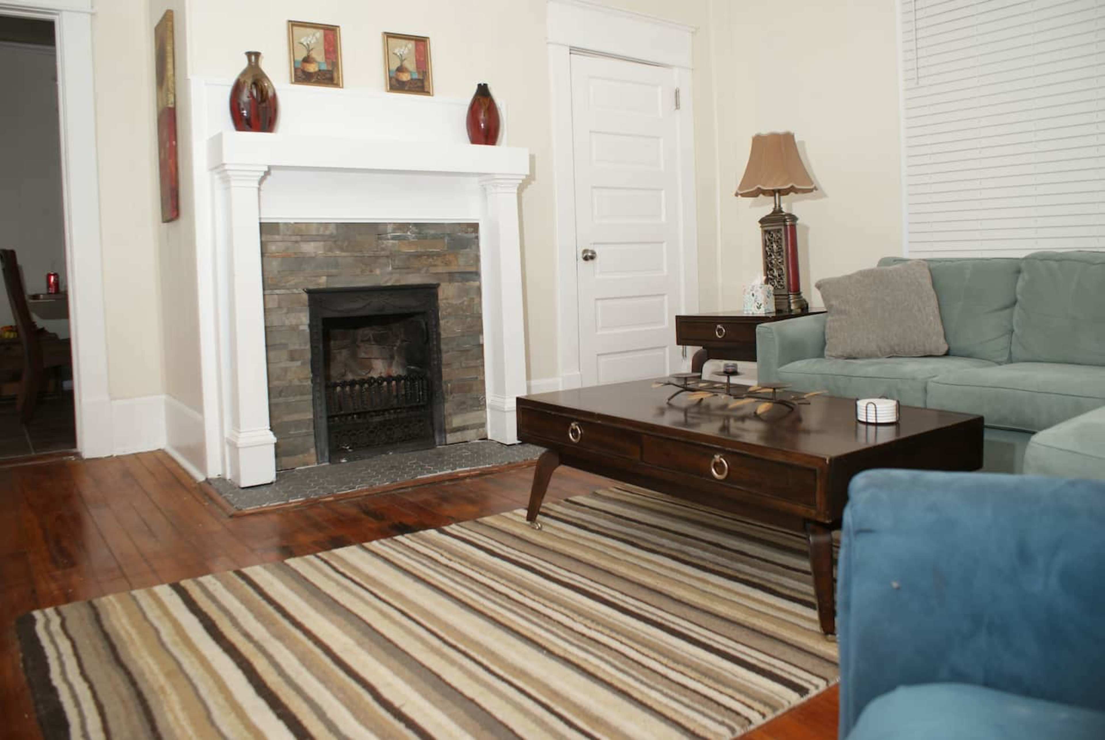 A living room with a stone fireplace, a wooden coffee table, and a blue sofa, all arranged on a striped rug.