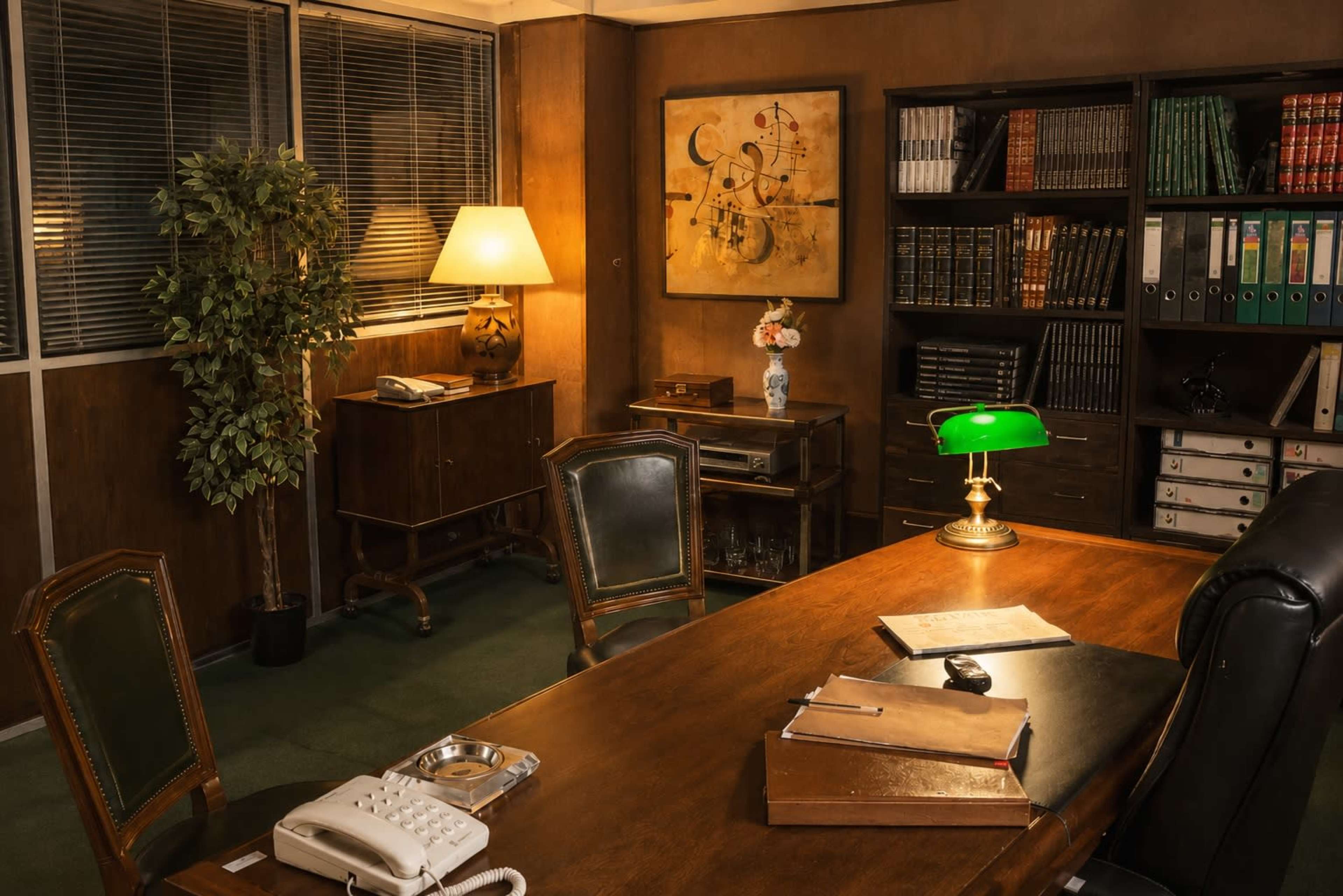 The image shows a dimly lit office with a wooden desk, an old-style telephone, a green desk lamp, and shelves filled with books and files.