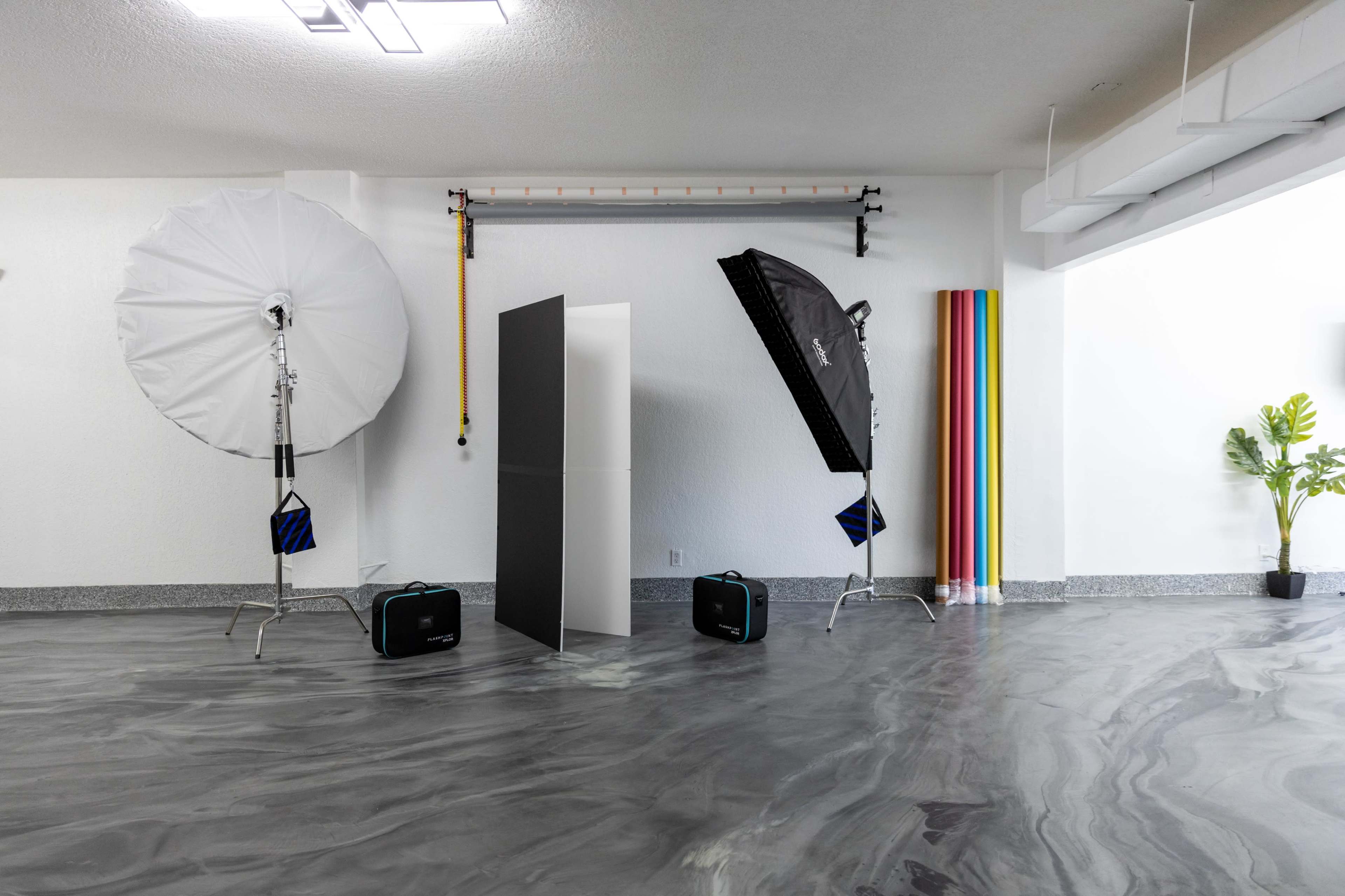 A photography studio with two large lighting umbrellas, a backdrop of colorful stripes, and an empty space on a polished floor.