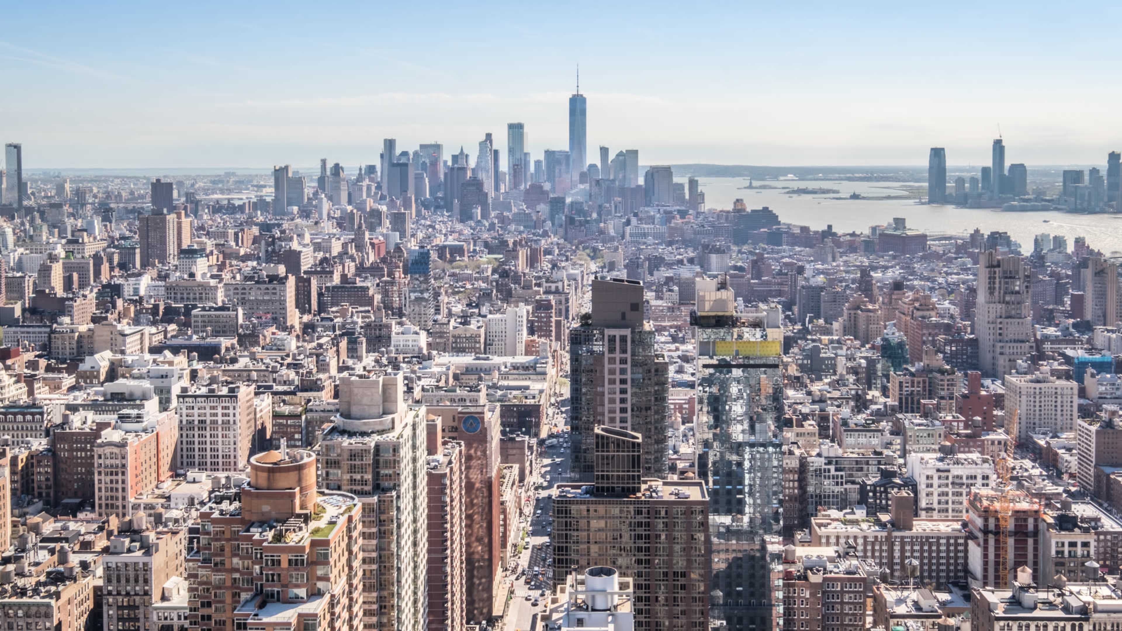 A panoramic view of New York City, featuring a dense skyline with skyscrapers and the One World Trade Center in the background.