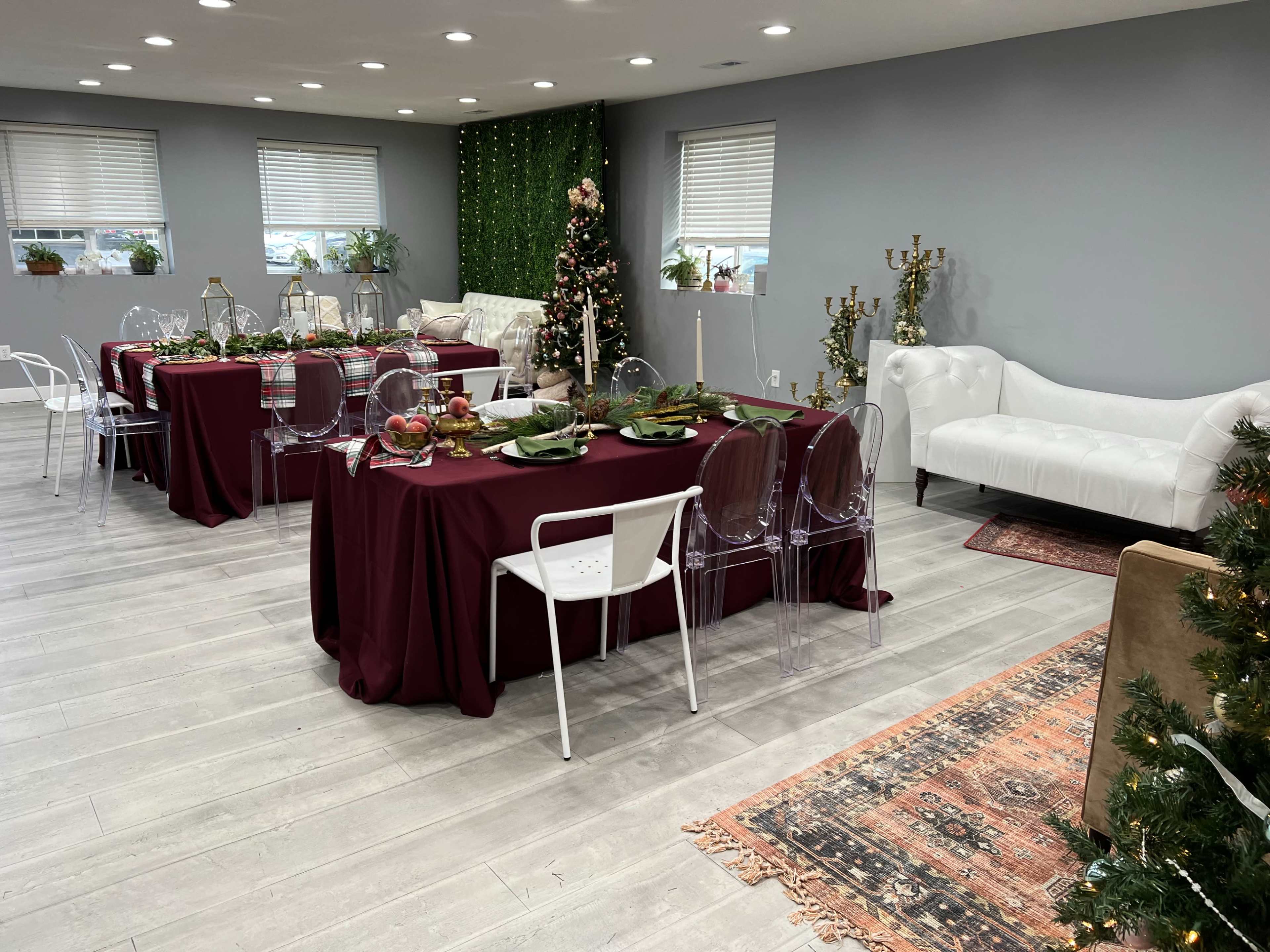 A decorated dining area featuring burgundy tablecloths, transparent chairs, a Christmas tree, and an arrangement of festive decor on the tables.