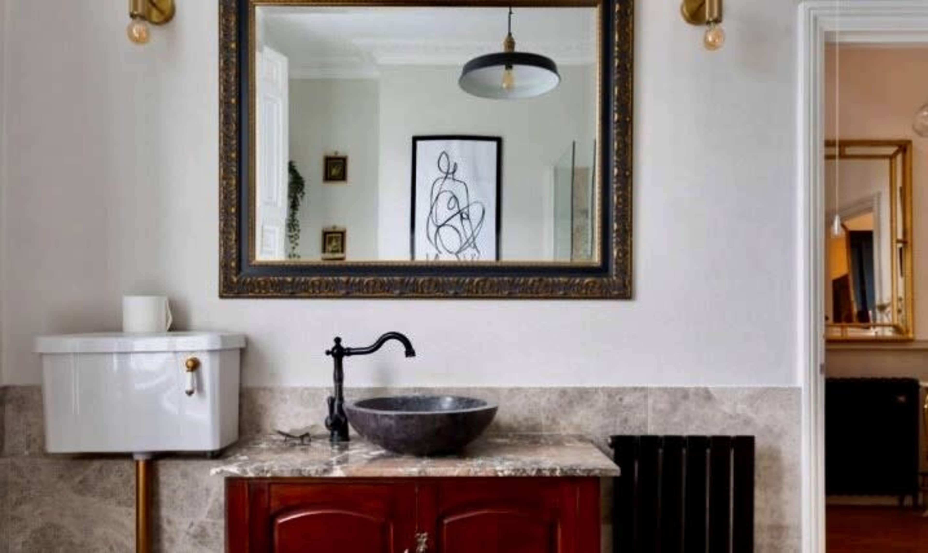 A bathroom with a round black basin on a marble countertop, a vintage-style toilet, a large framed mirror, and a pendant light hanging above.