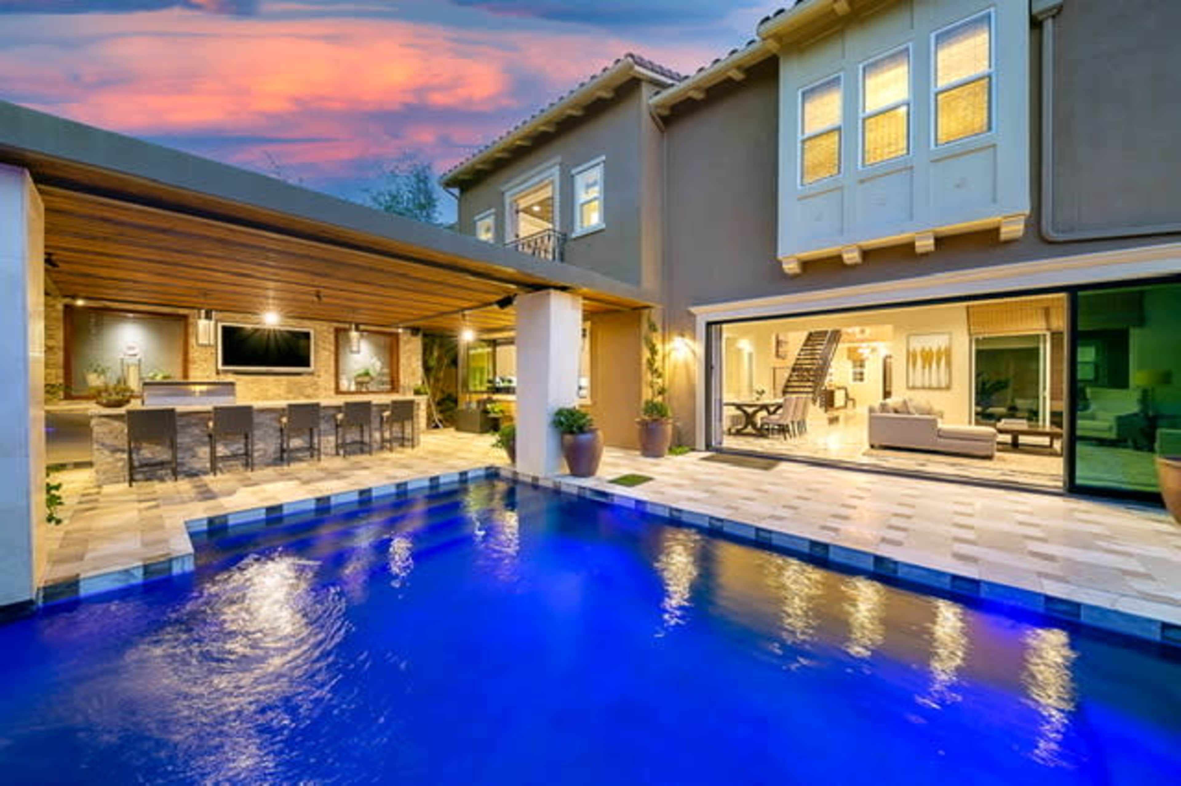 A modern backyard with a swimming pool, an outdoor bar area, and a stylish home with large windows.