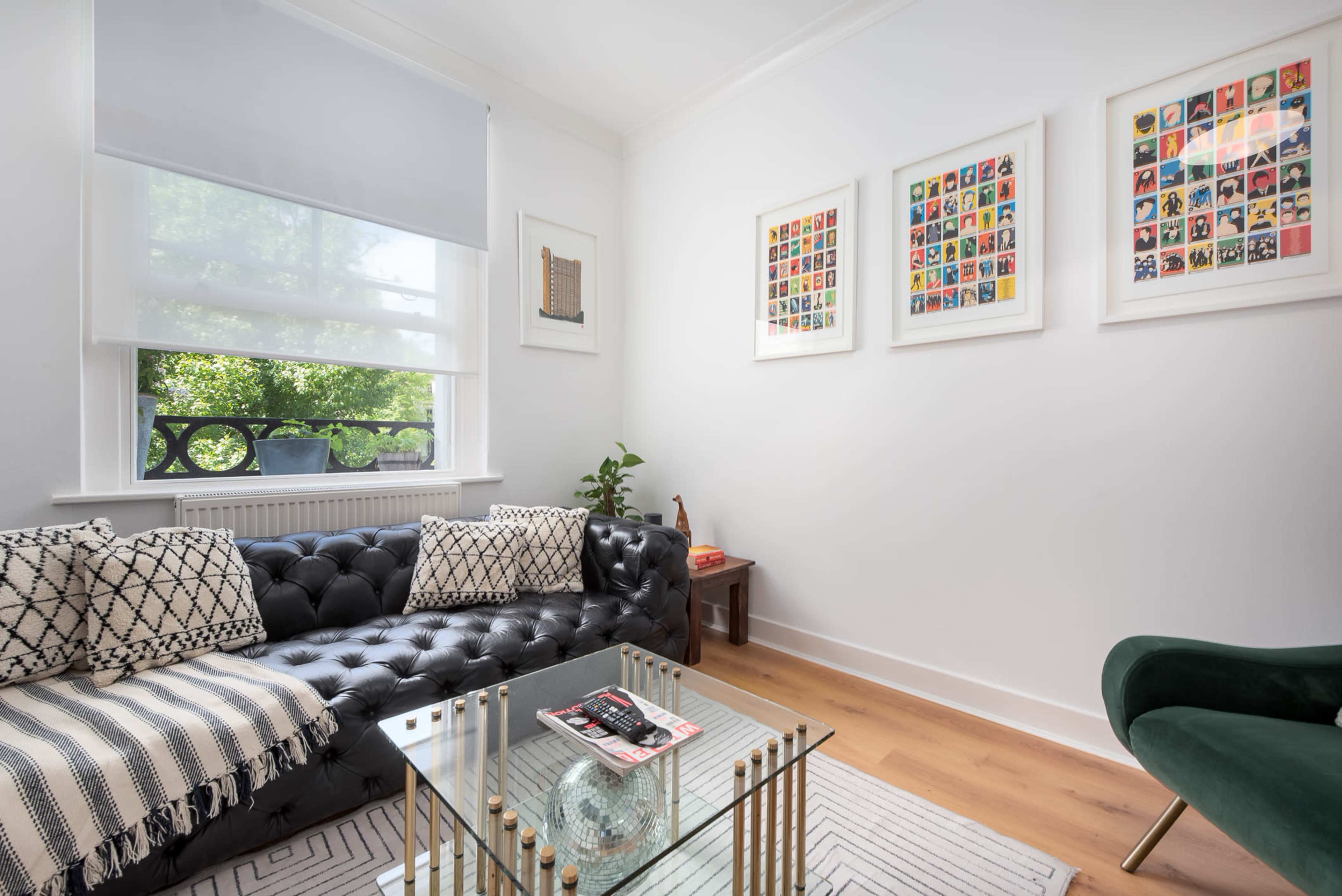A modern living room with a black tufted sofa, a glass coffee table, and colorful framed artwork on the walls.