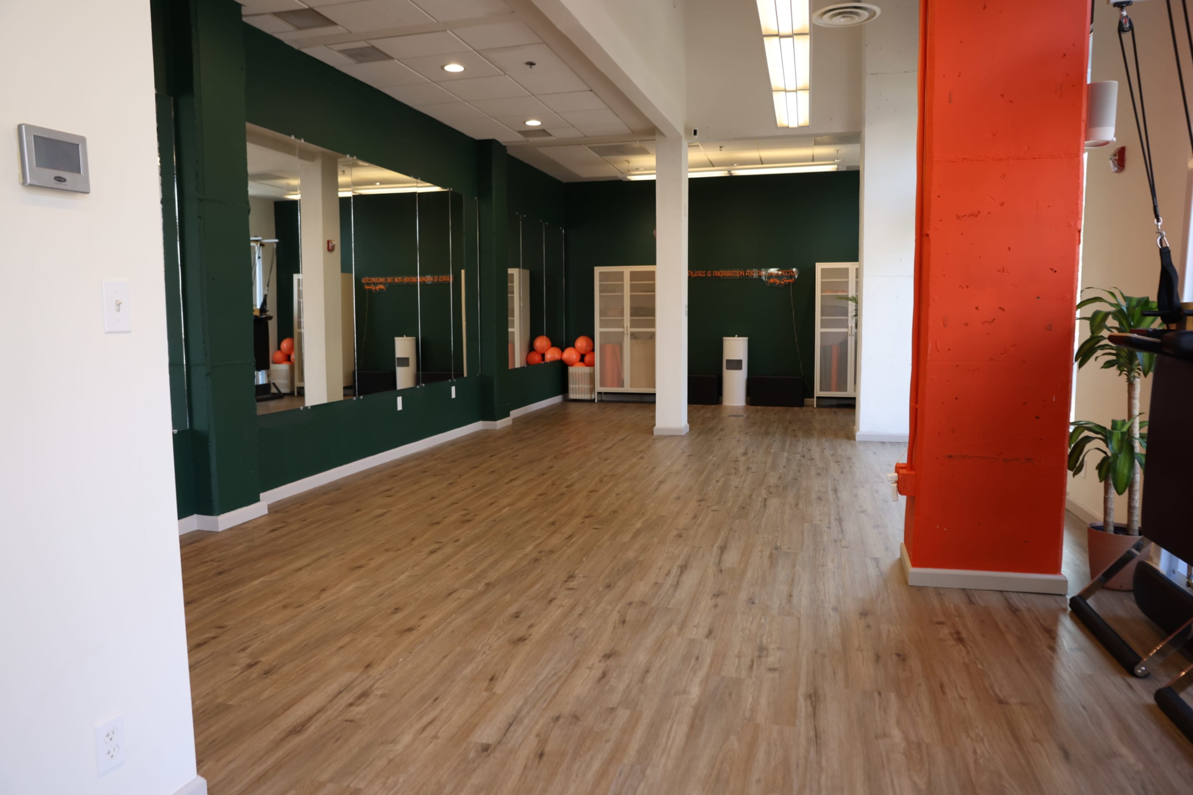 The image shows a spacious workout studio with green walls, wooden flooring, and fitness equipment neatly arranged along one side.