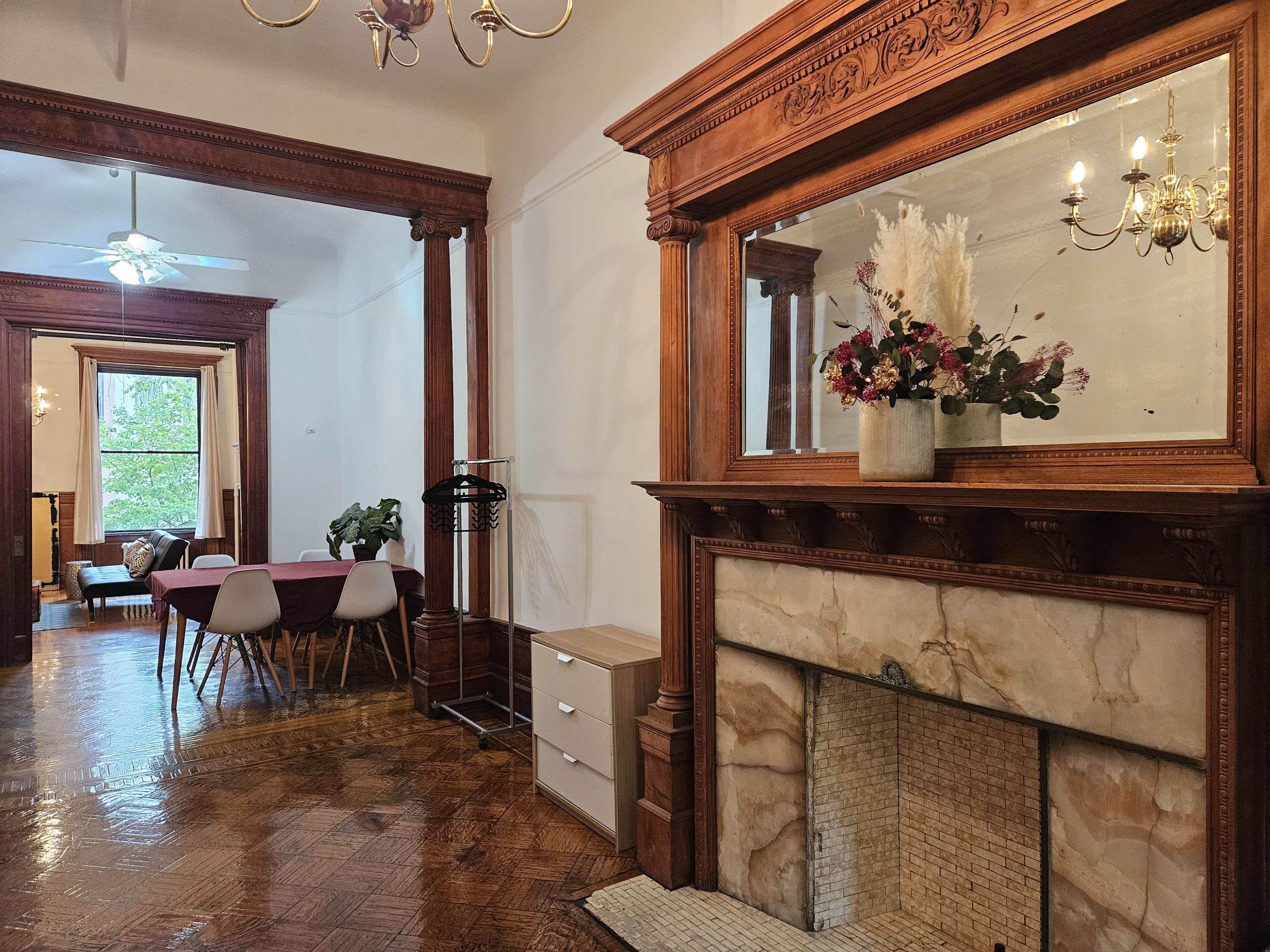 A spacious interior with a wooden mantel, a decorative mirror, and a dining area featuring a pink table and various chairs.