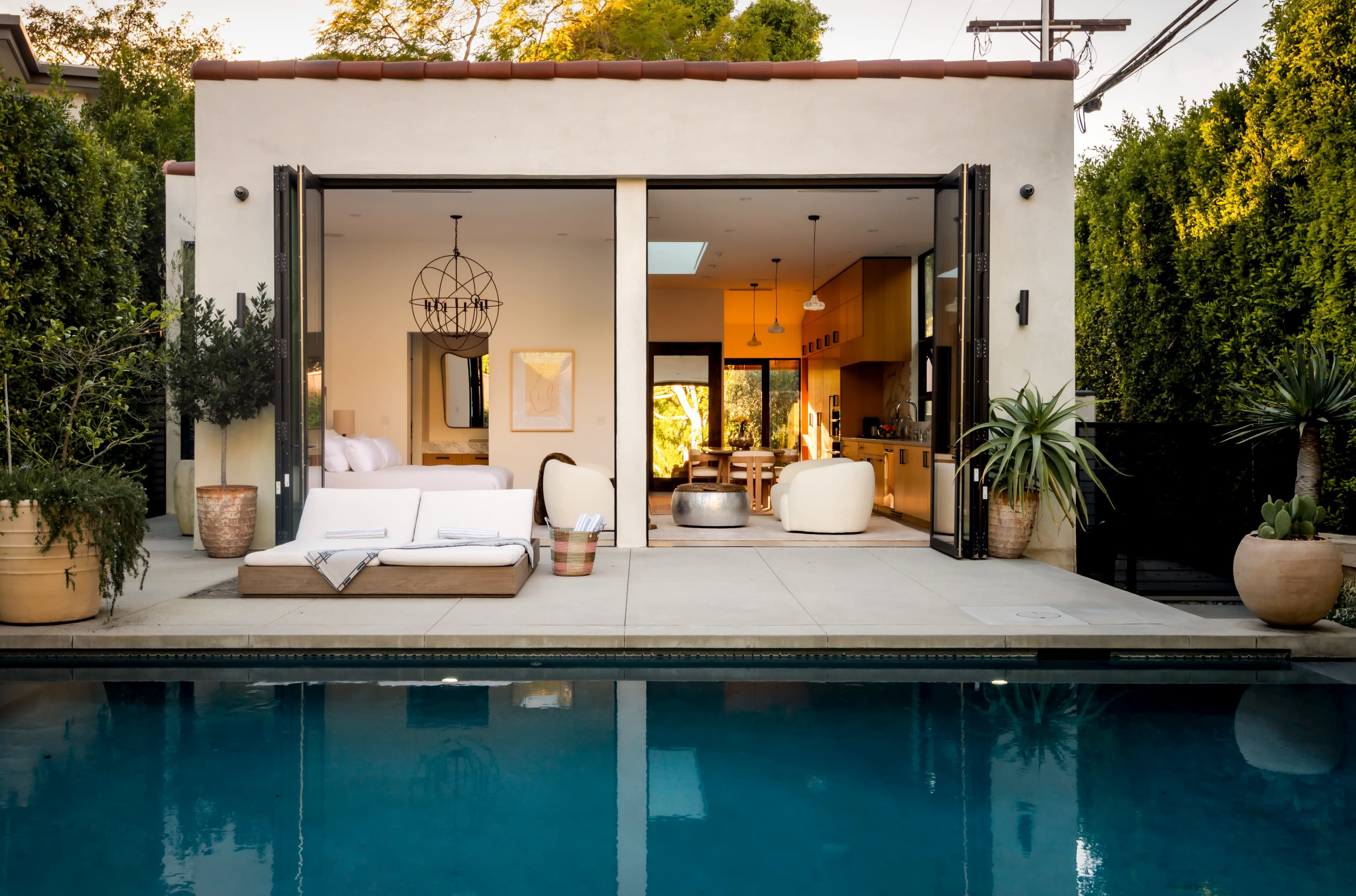 A modern home features large sliding doors opening to a patio with seating and a pool, surrounded by greenery.
