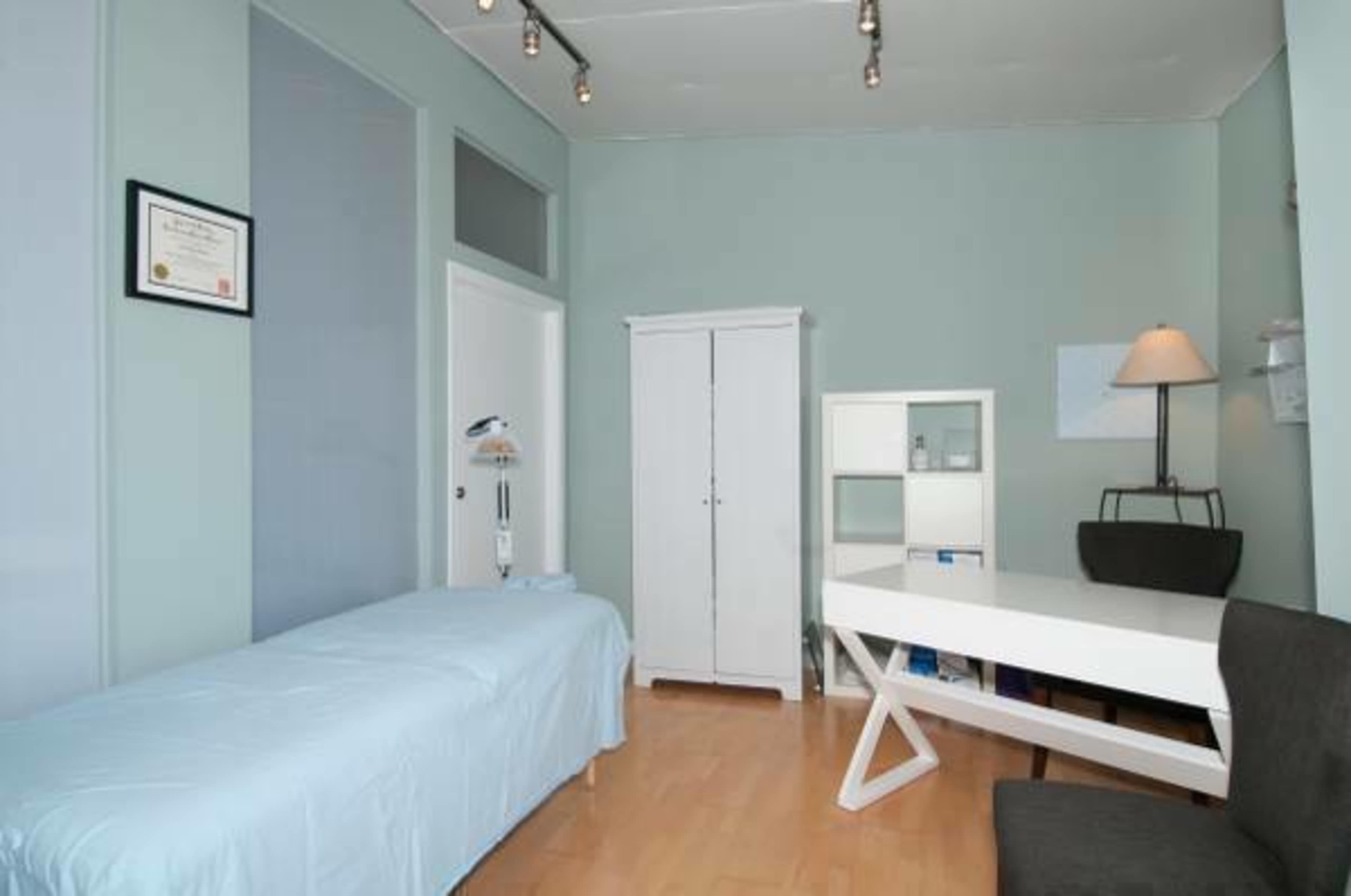 A small room with a treatment table covered in a light blue sheet, a white cabinet, a desk, and a chair.