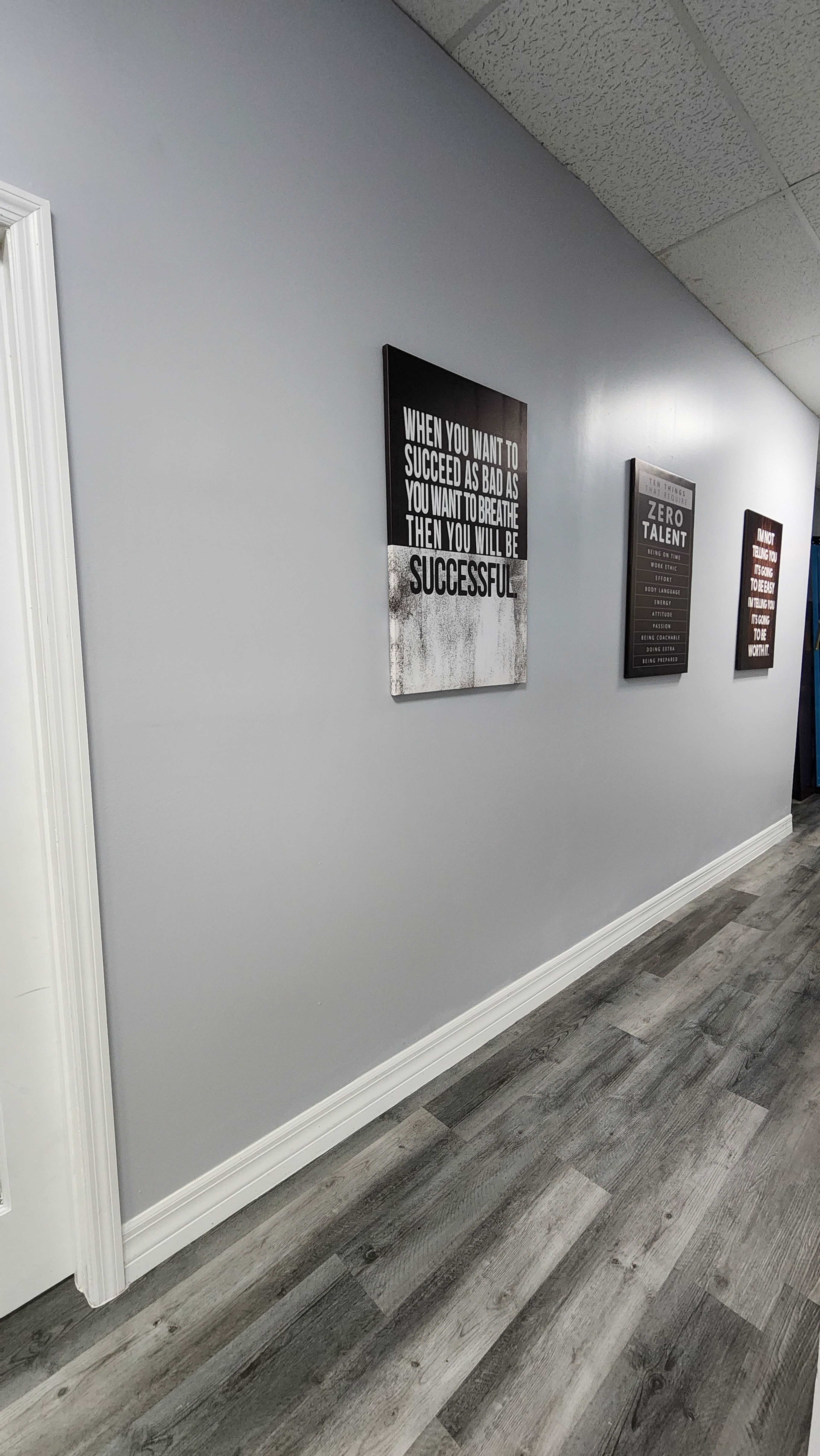 The image shows a hallway with light gray walls featuring motivational wall art and laminate flooring.