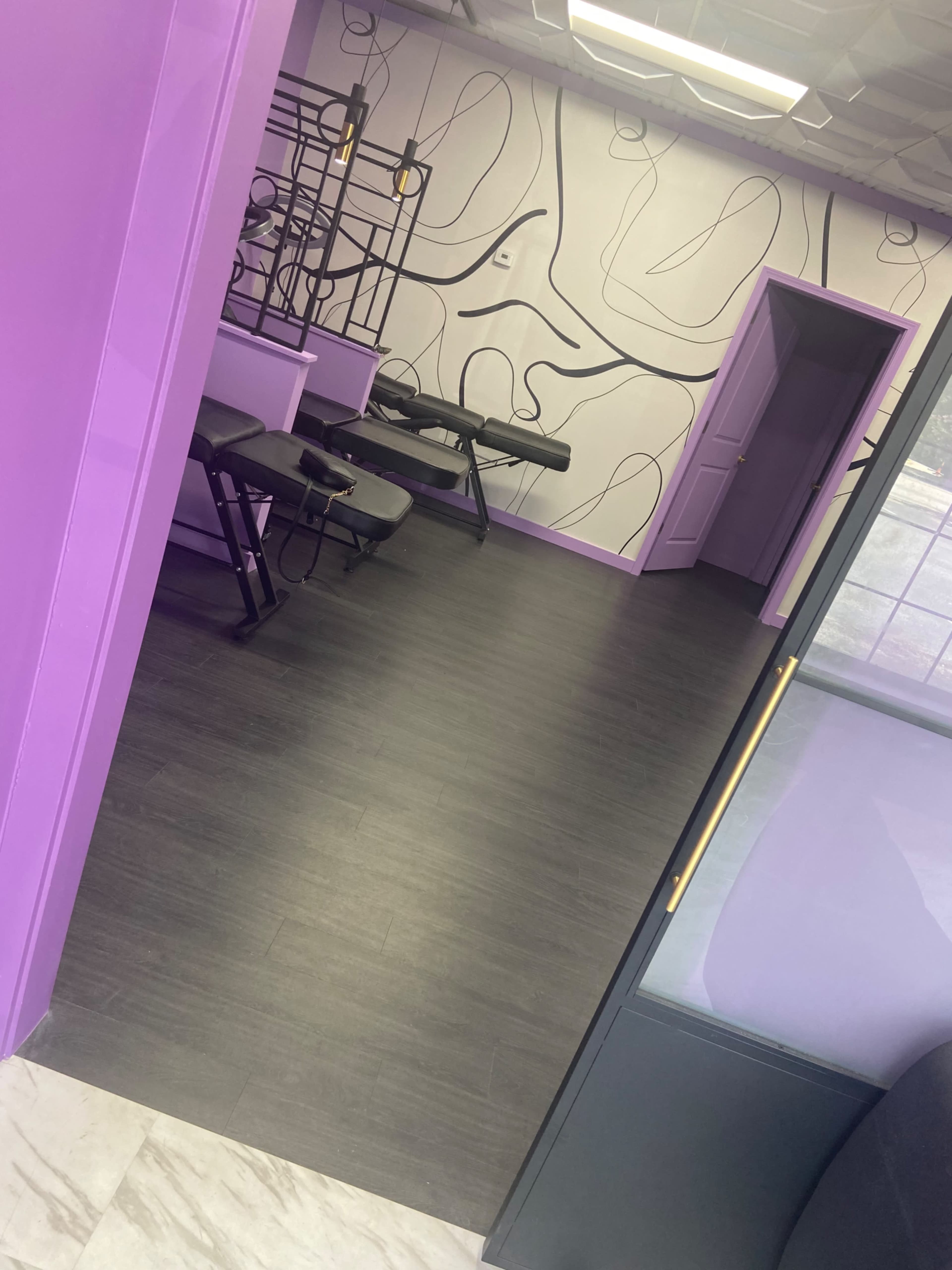The image shows a salon or spa interior with purple walls, a patterned mural, and black treatment chairs arranged in the space.